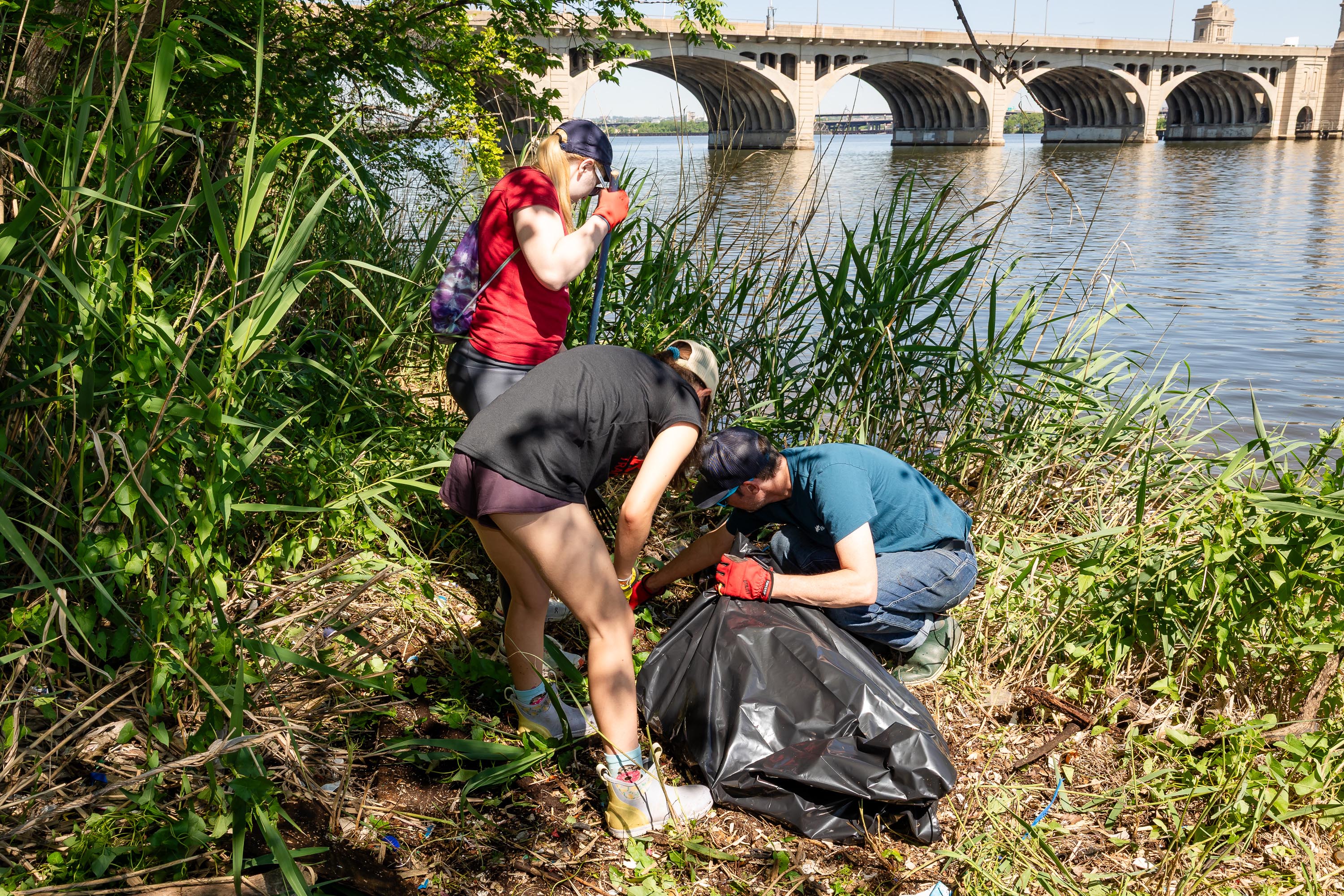 A team bagging up trash along the water with Hanover St Bridge in background.