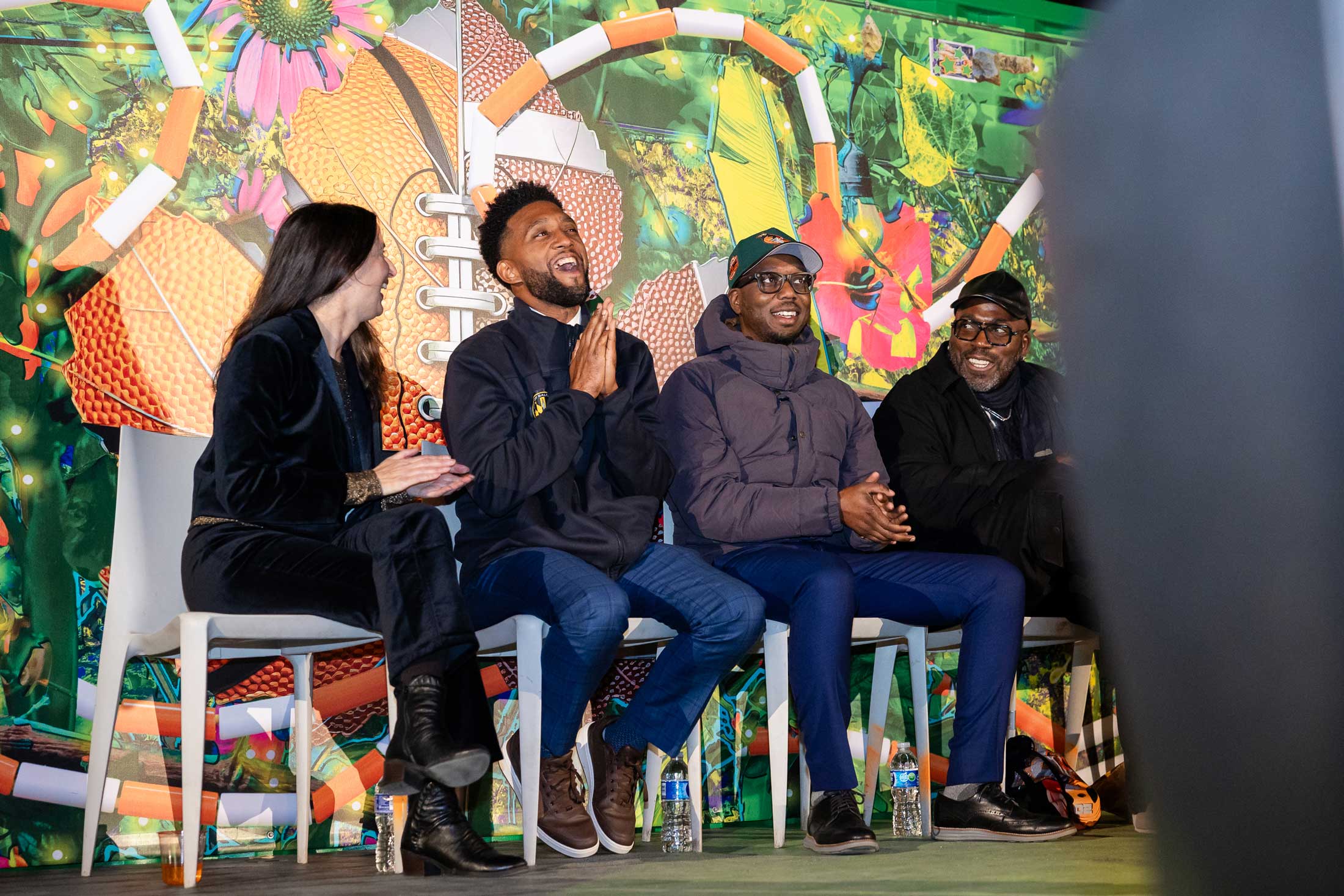 Soft Gym by Wickerham and Lomax, an Inviting Light installation at YNOT LOT in Station North Arts District. Speakers laugh on stage against colorful mural, including Baltimore mayor Brandon Scott.
