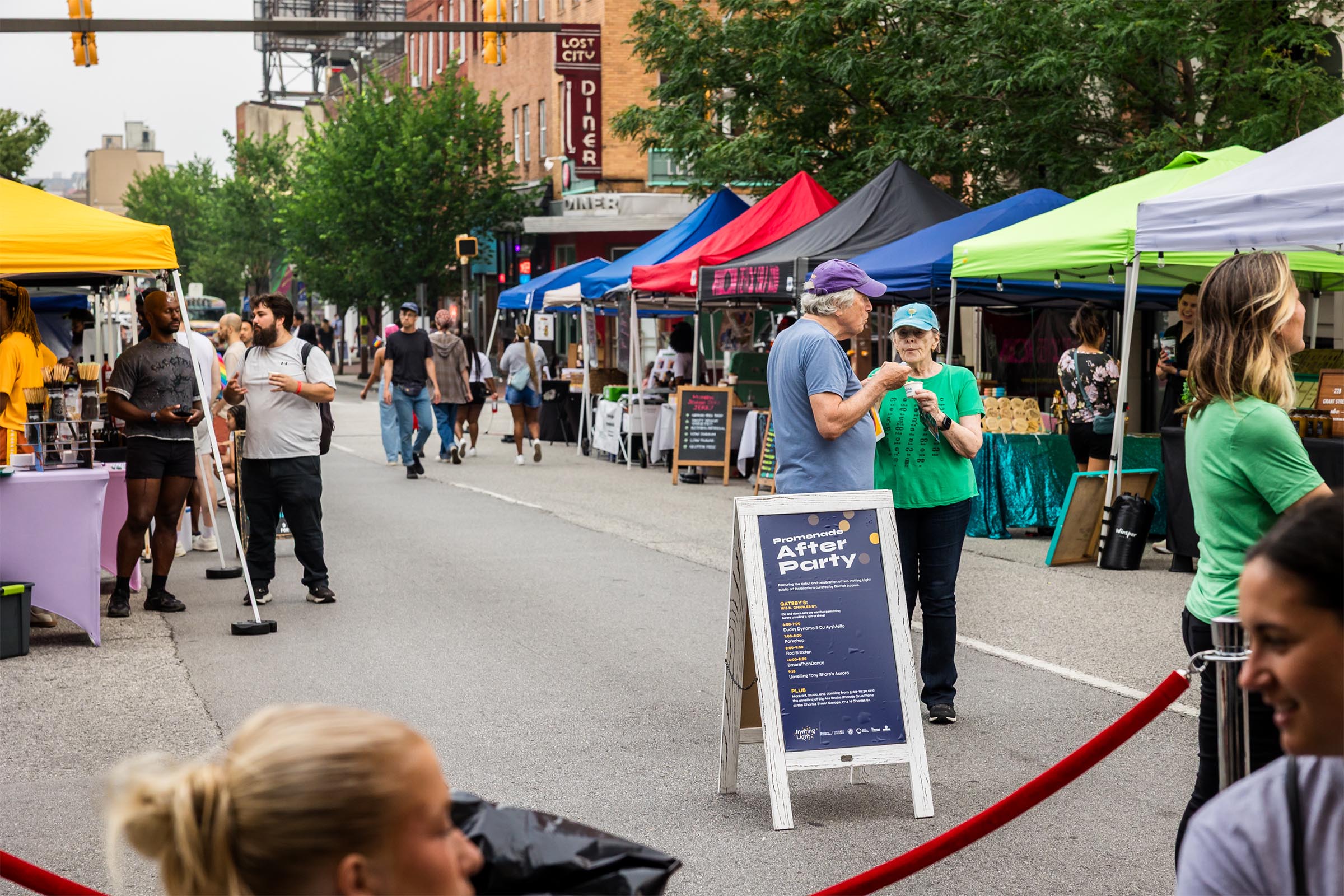 A closed down Charles Street during Pride after party open to foot traffic. People from all walks of life mingle and stroll along booths of art, local goods, and food.
