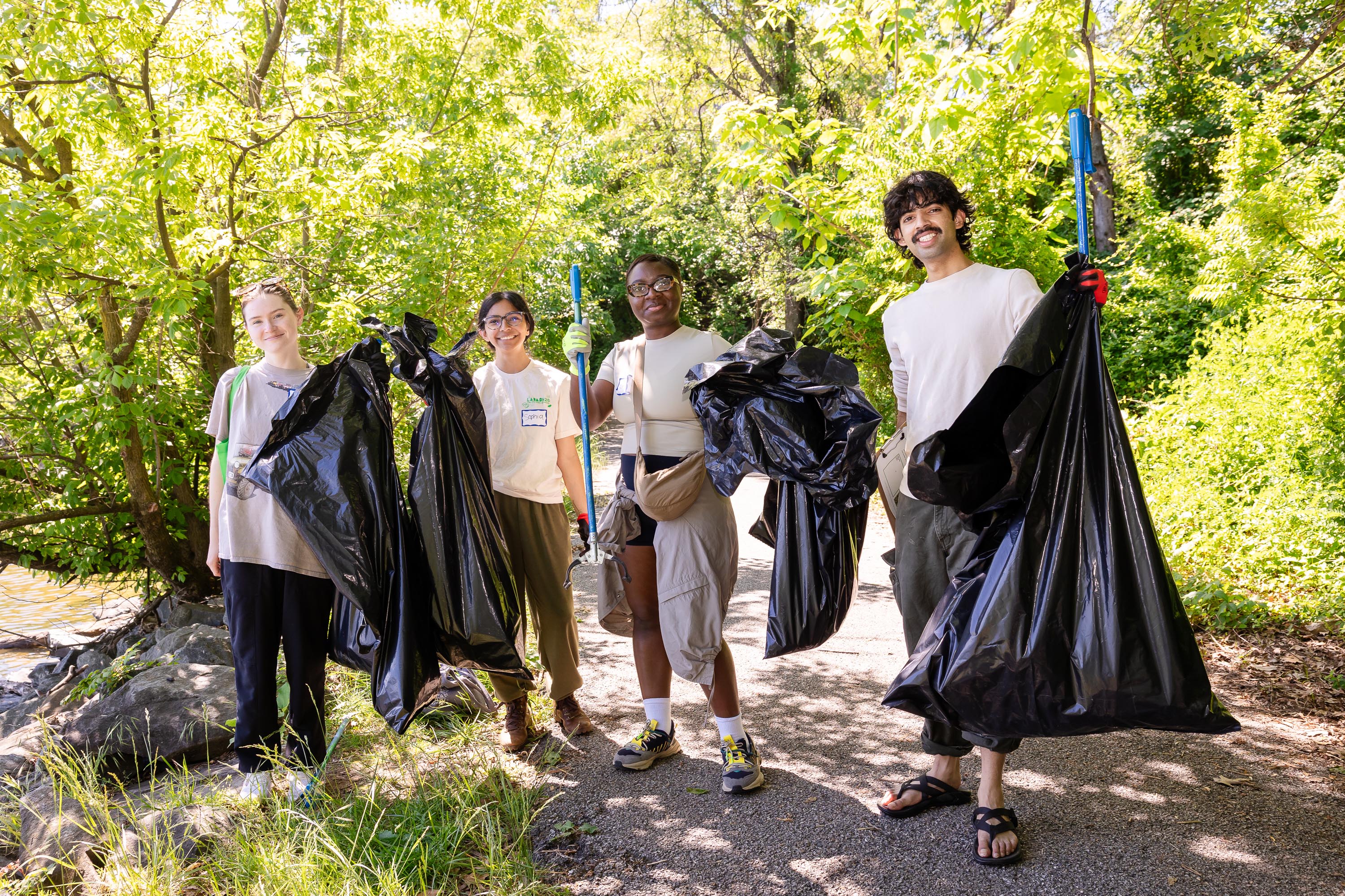 Four young participants smile and pose on wooded path with their trash bags and grabbers.