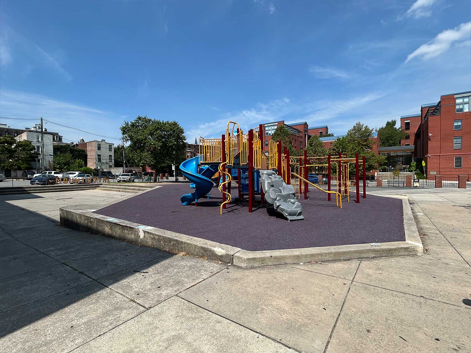 Mt. Royal Existing Playground showing a medium-sized metal playground on patch of astroturf surrounded by concrete surfaces.