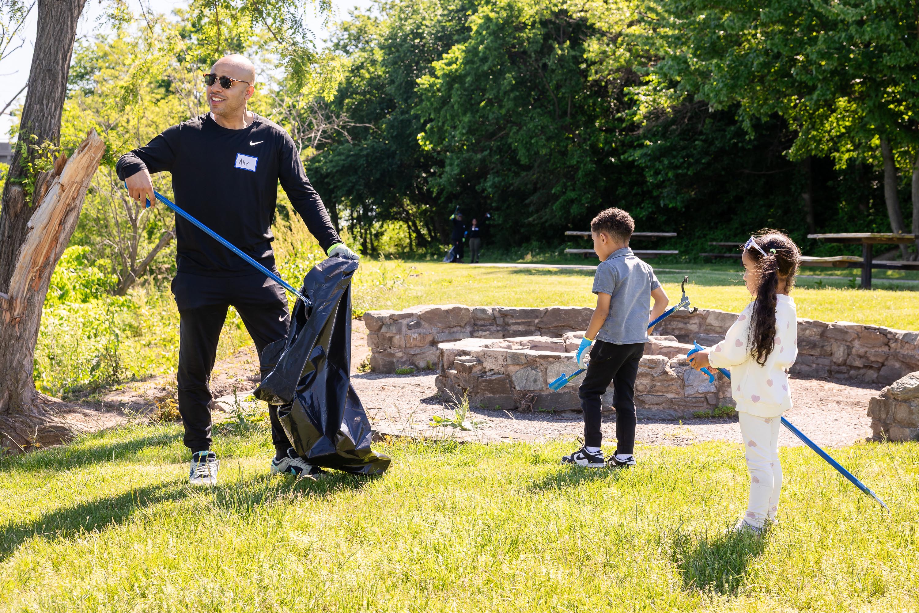Family with little kids picks up trash in field.