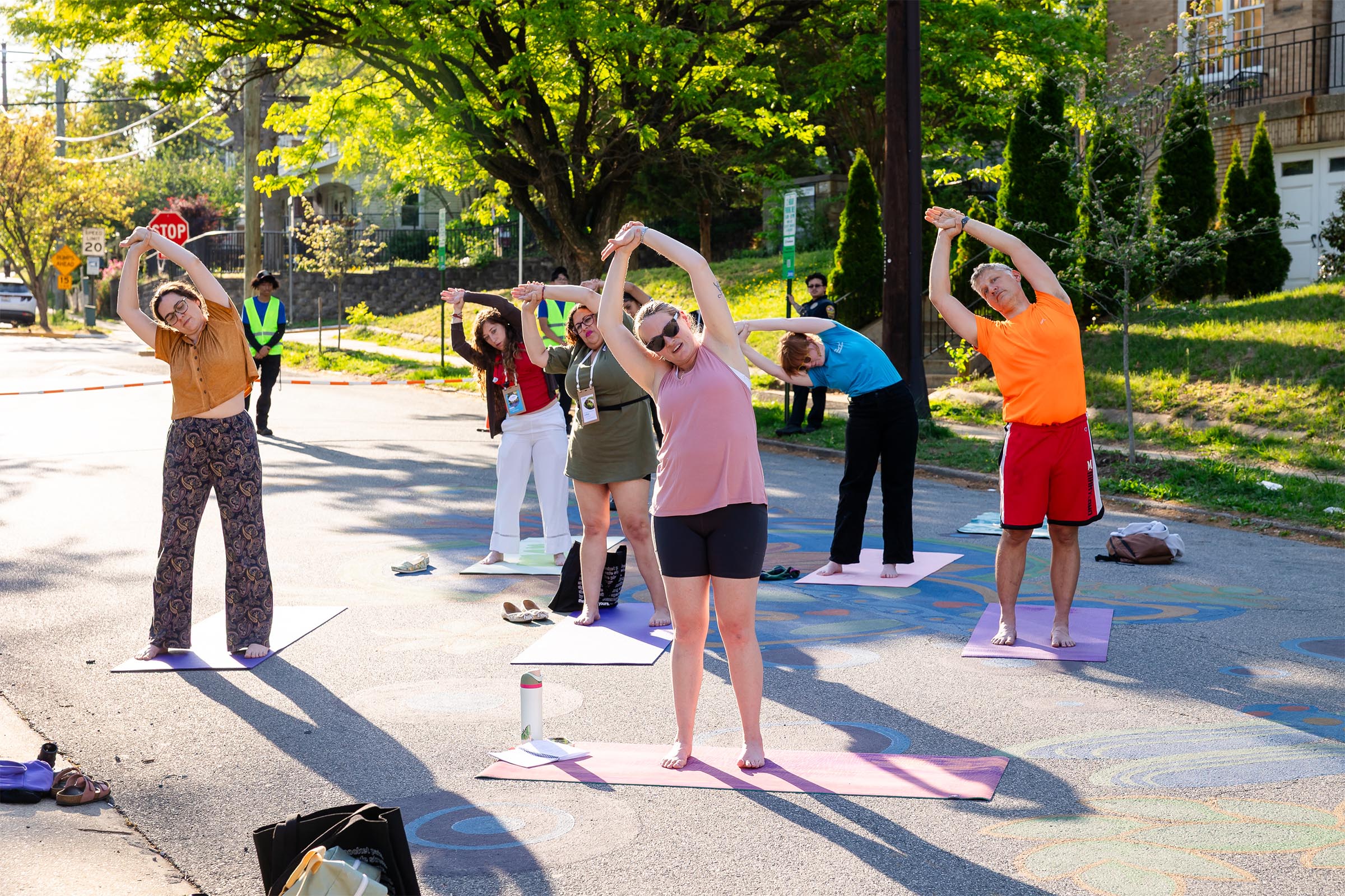 Participants of The Vision is Yours Placemaking and Placekeeping Conference 2026 do yoga in the street, slowing down a normally busy Bunker Hill Road and making space for human connection. 