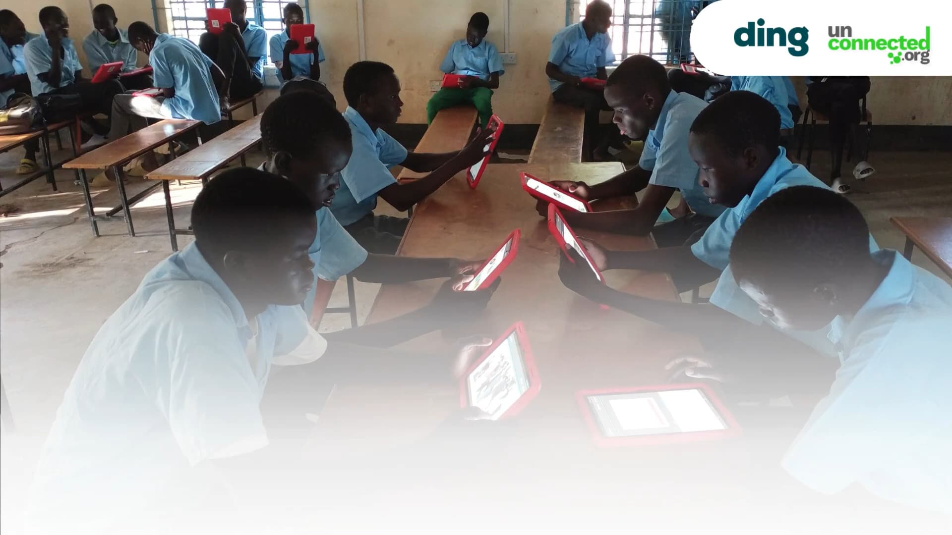 A group of students in a classroom, wearing light blue uniforms, are seated at wooden desks. They are focused on using tablet devices. The room has windows with bars and appears to be well-lit. The logos of "ding" and "unconnected.org" are in the upper right corner of the image.