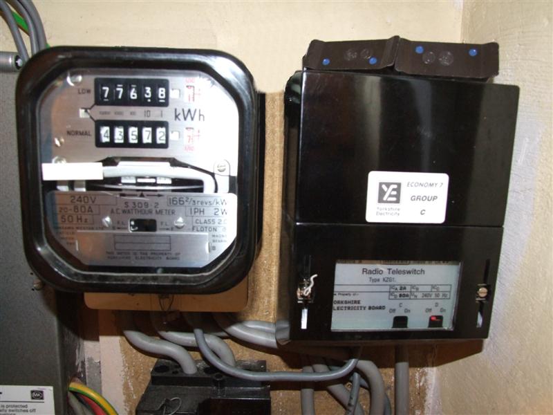 An RTS meter on the left  with a radio teleswitch on the right in a black box mounted on a wall. The black box is rectangular with the shorter sides at the top and bottom. It has some grey cables coming out of the bottom of it, some of them go to the RTS meter on the left. The front of the box has a glass window at the bottom. Behind the window there is a silver panel that has radio teleswitch printed on it and some numbers and text that aren’t clear in the image.

The RTS meter to the left of the radio teleswitch box has a row of 6 numbers displayed on the front near the top. The numbers  tell you how much electricity has been used - for example, this meter shows 71462.3. Below the numbers are the letters kWh.
