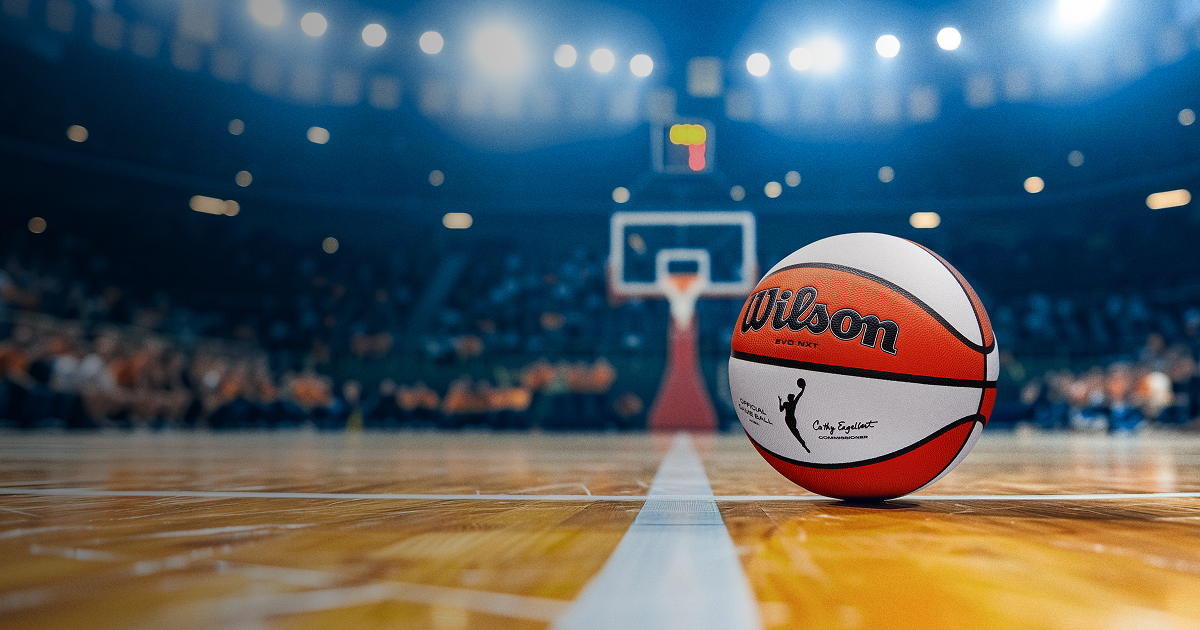 A Wilson WNBA basketball rests on a professional hardwood court under bright arena lights, creating a premium hero image for Fanatics Sportsbook WNBA betting and live game action.