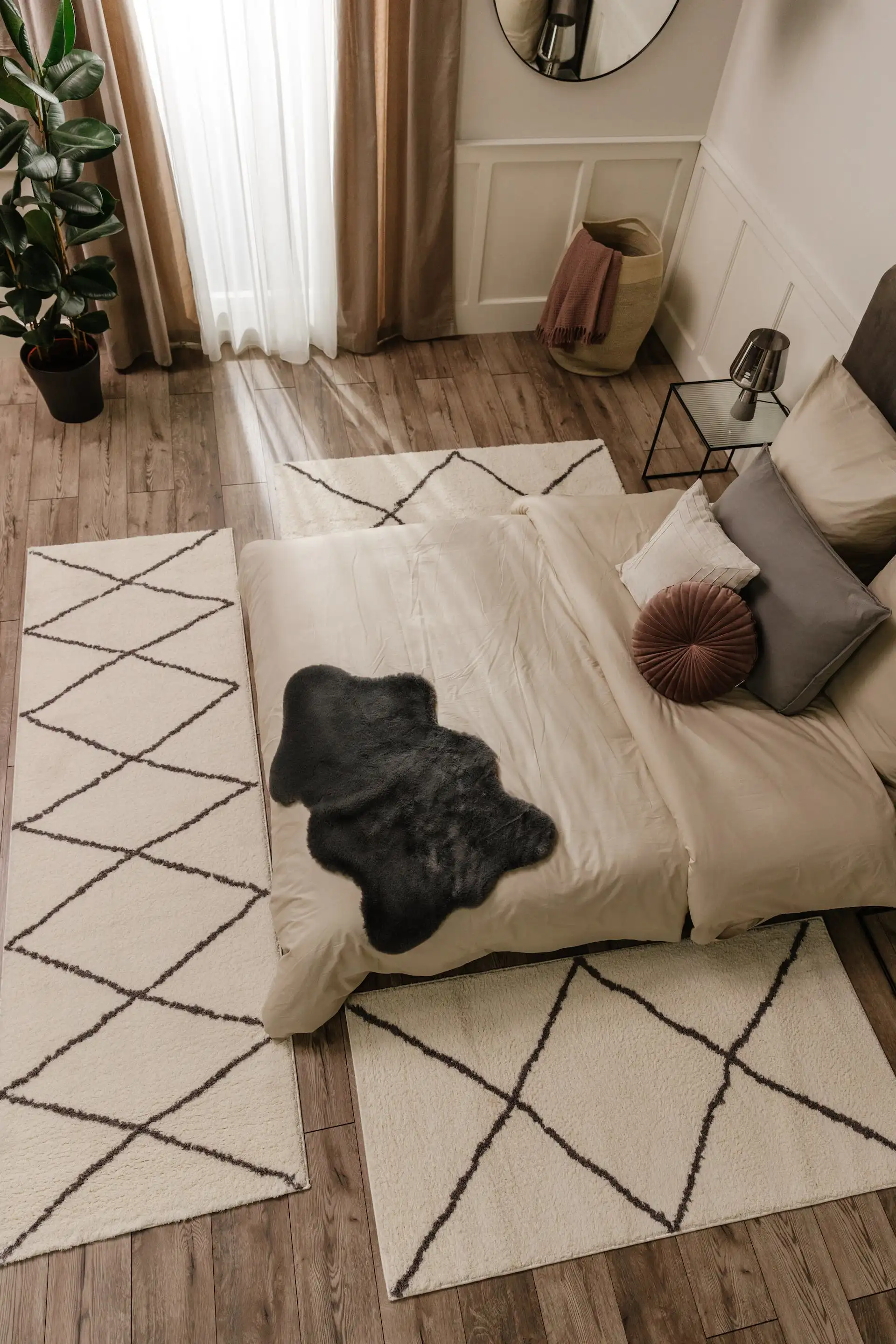 Schlafzimmer von oben eingerichtet mit zwei Kelim-Teppichen als Bettvorlegern, einem großen Boxspringbett in Grau, zwei schwarzen Beistelltischen und einer großen Topfpflanze