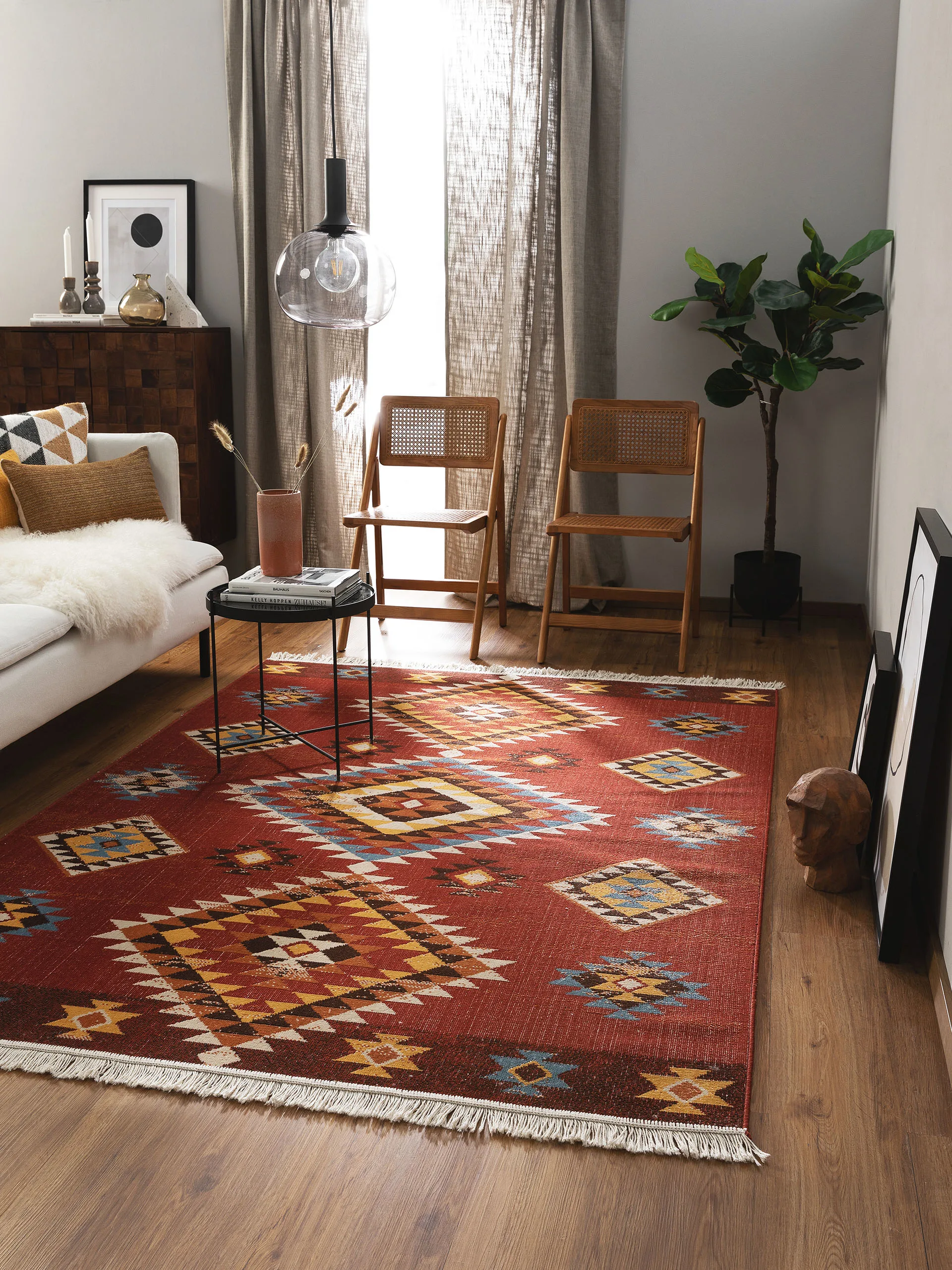Schlafzimmer im Ethno Style mit einem roten Teppich im Kelim-Design, Pflanzen und Möbeln in natürlichen Brauntönen