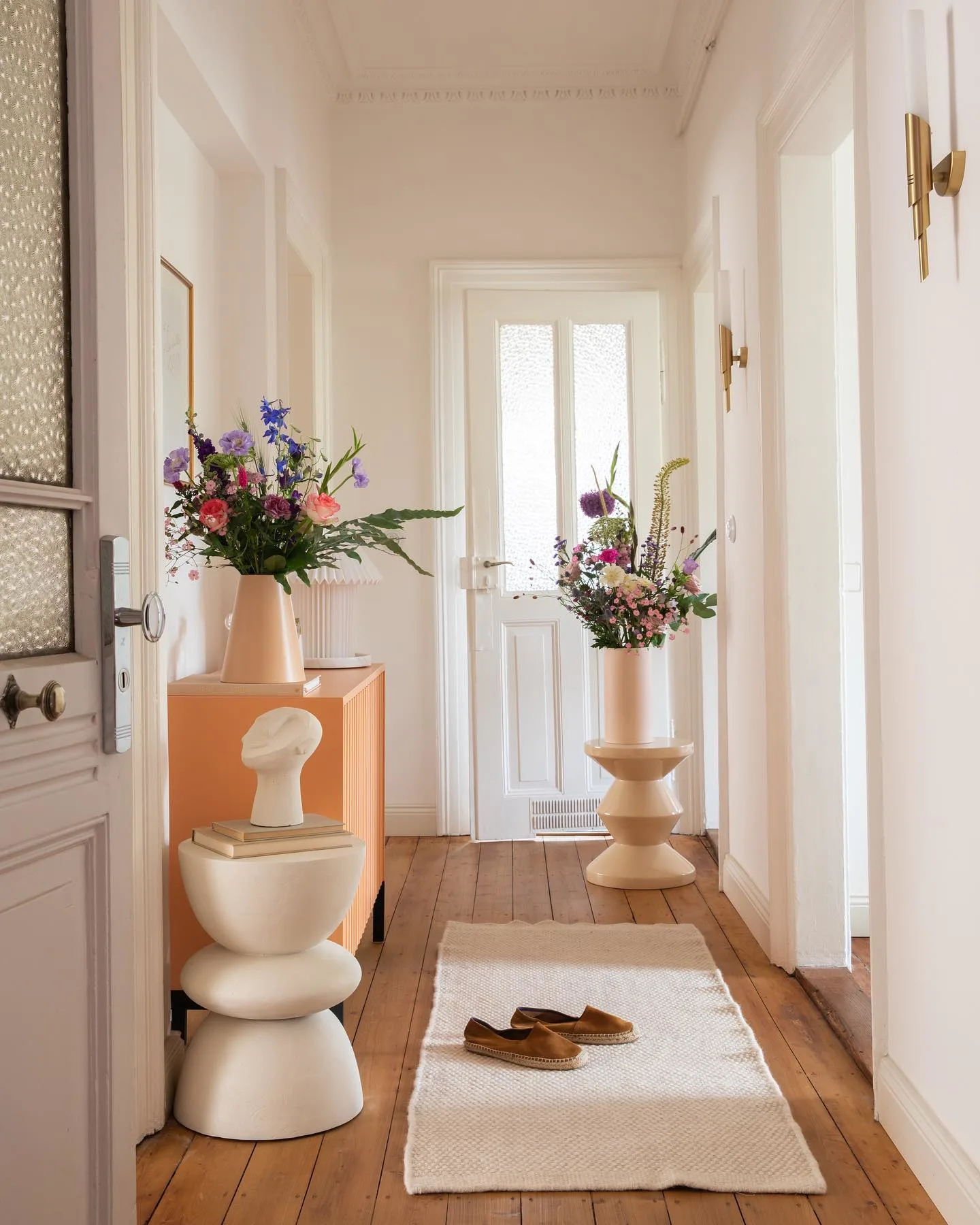 Einladend gestalteter Flur mit hellem Teppichläufer auf braunem Parkettboden, modernen Beistelltischen und großen Vasen mit frischen Schnittblumen