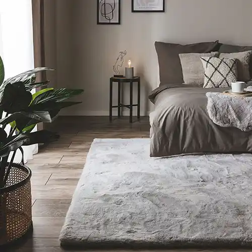 Hochflorteppich in Grau, auf dem die Hinterbeine eines Bettes stehen, um so im Schlafzimmer die richtige Teppichgröße zu haben
