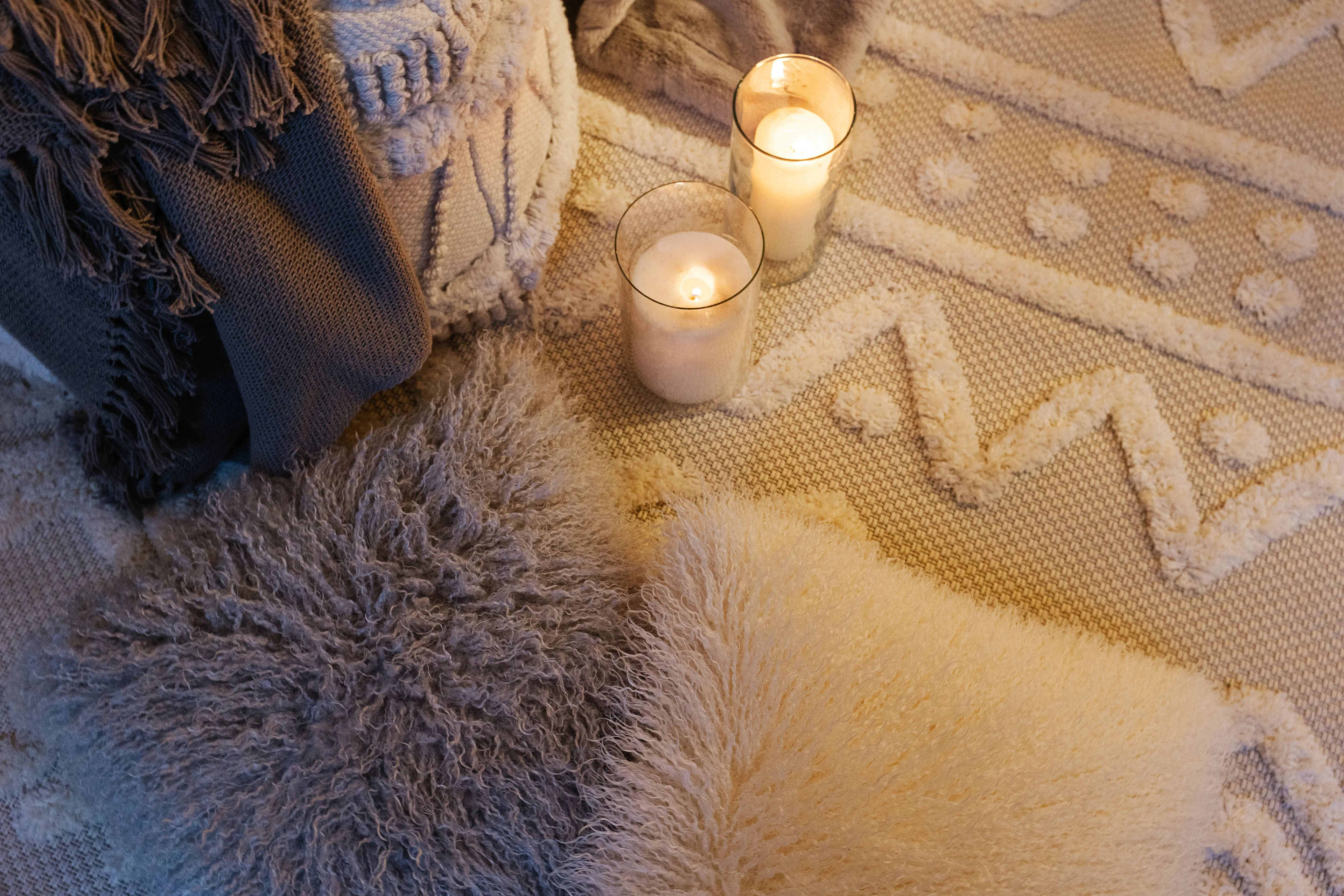 Detailaufnahme von einer Weihnachtsdekoidee mit Kerzen, flauschigen Kissen in Grau und Beige und einem gemütlichen Sitzpouf in einer Ecke