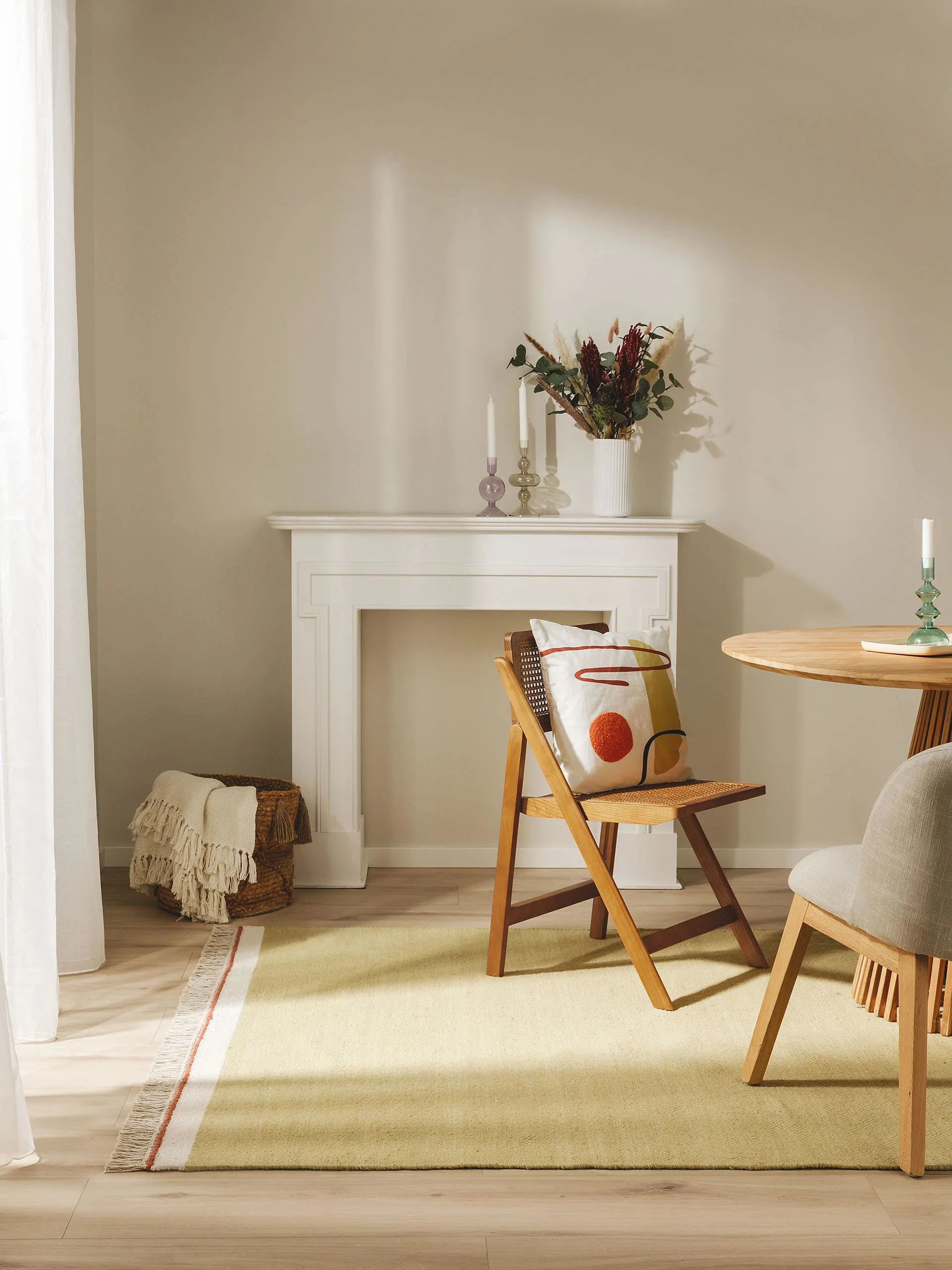Kleines Esszimmer eingerichtet mit einem runden Holztisch und zwei Holzstühlen auf einem hellgrünen Teppich mit weißen Fransen