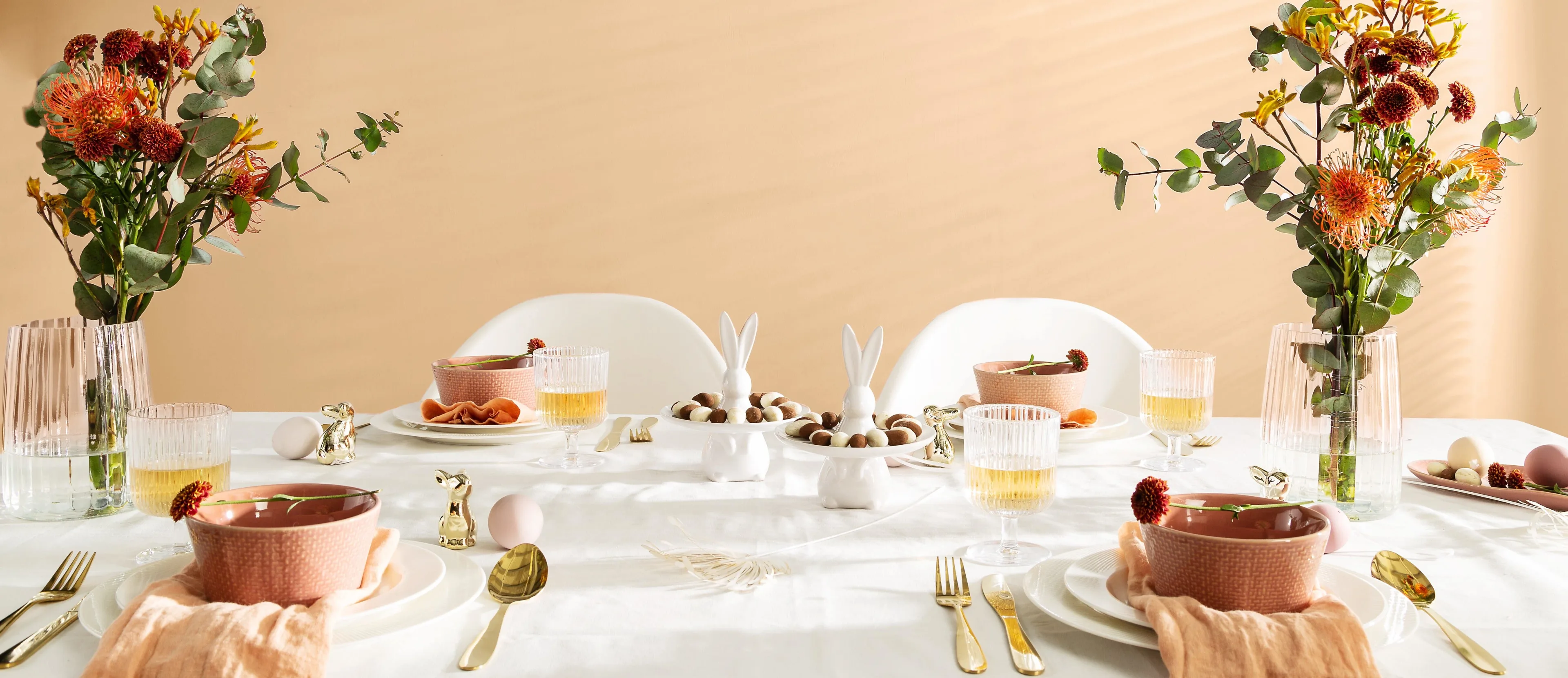 Osterdeko mit weißen Tellern, goldenem Besteck und weißen Servierschalen in Häschenform gefüllt mit süßem Gebäck