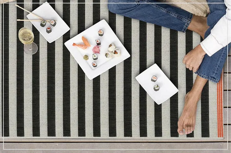 Foto von oben von einem schwarz-weiß gestreiften Outdoor-Teppich auf dem Balkon mit drei Tellern mit Sushi und Stäbchen