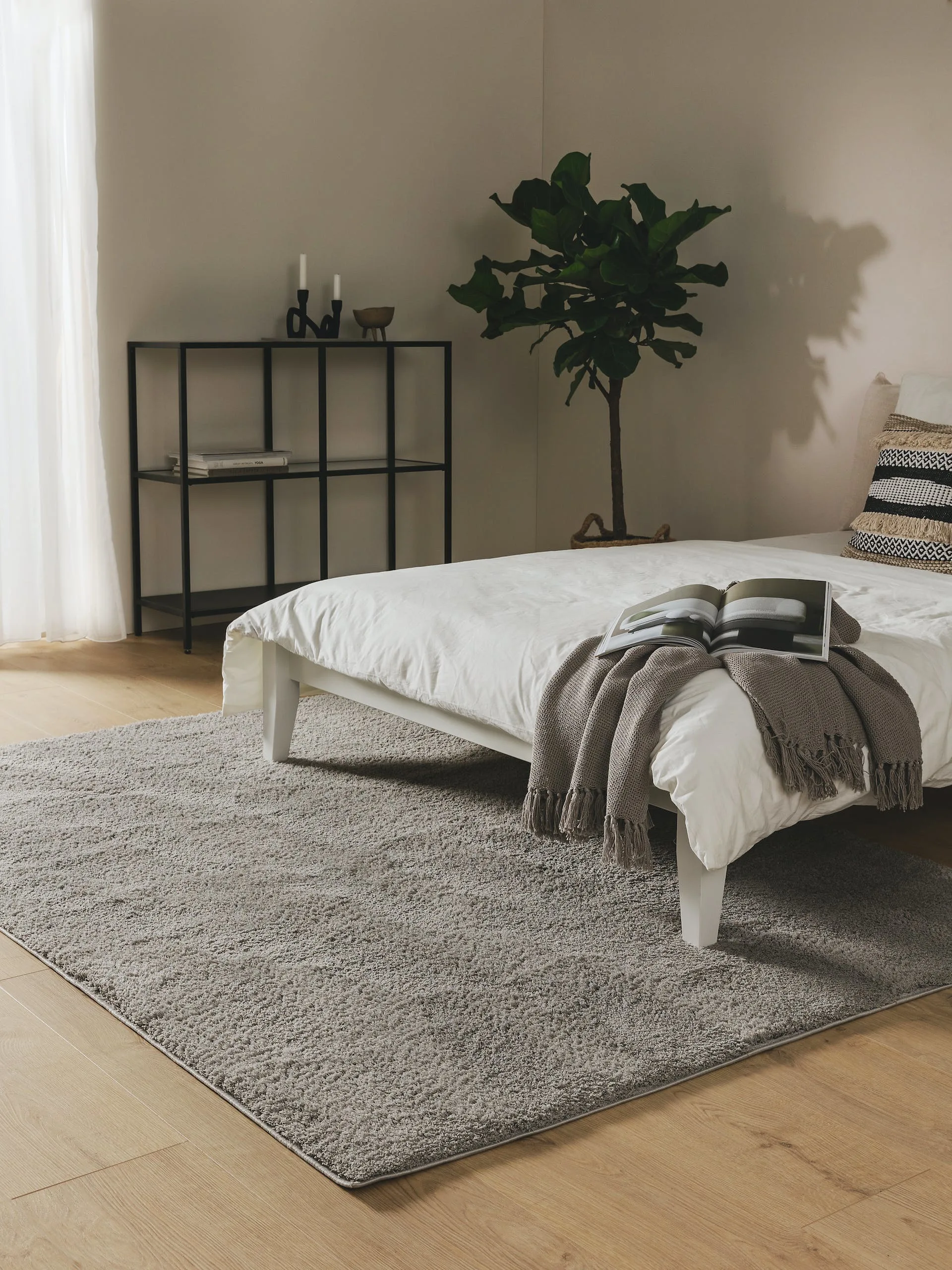 Schlafzimmereinrichtung im Industrial Chic mit weißem Bett, schwarzem Regal aus Metall und einem großen, grauen Shaggy-Teppich als Bettvorleger unter dem Bett