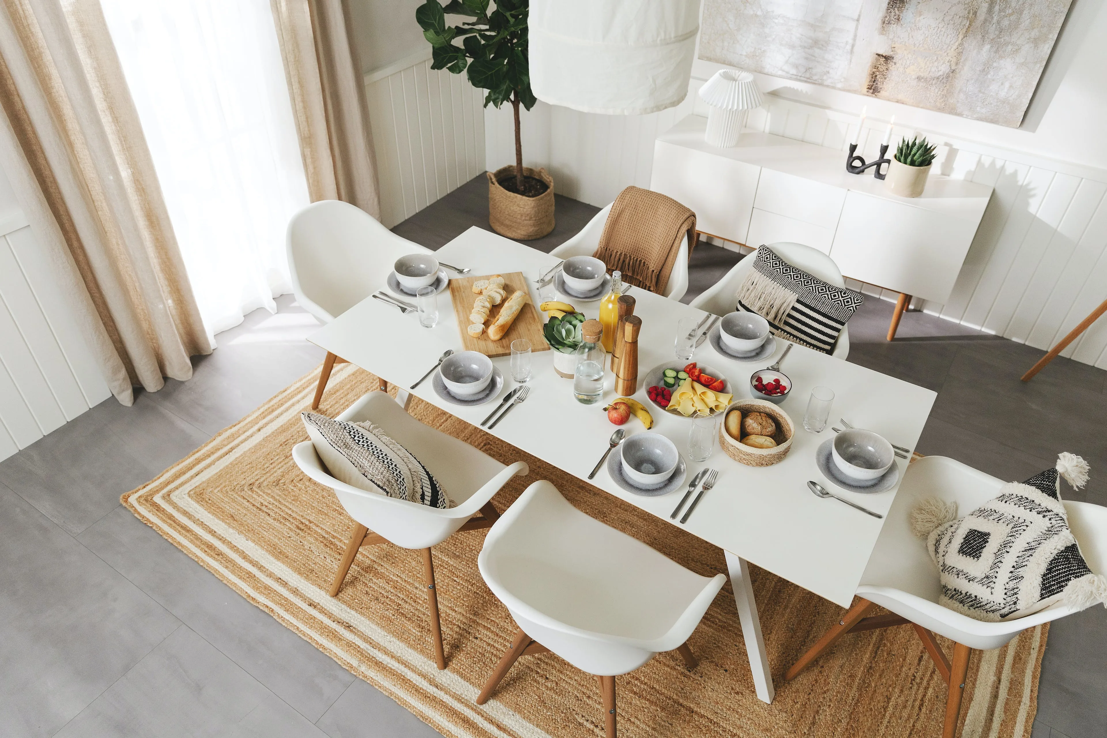 Aufnahme von oben auf den gesamten, weißen Tisch in einem Esszimmer, der für einen Frühstücksbrunch gedeckt ist mit Aufschnitt, Brötchen, Obst und Gemüse