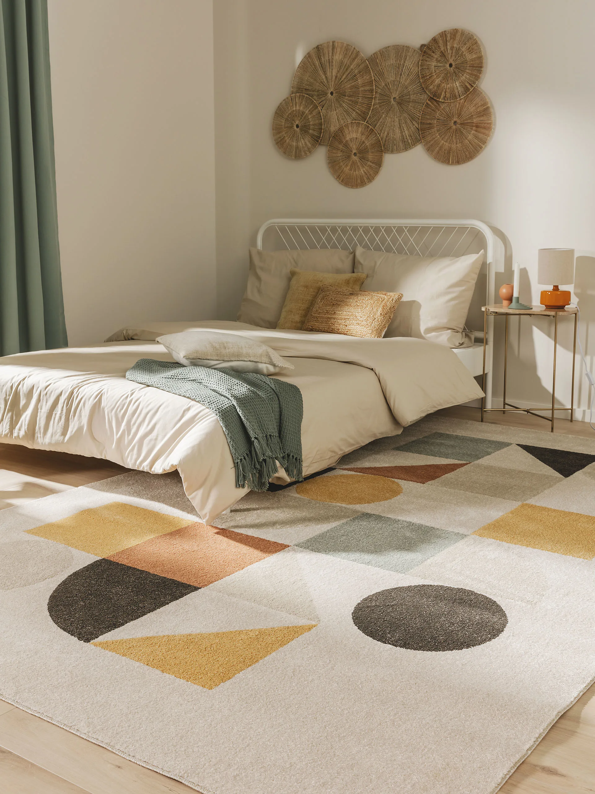 Natürlich eingerichtetes Schlafzimmer mit Farbakzenten: Ein Teppich in Mintgrün, Gelb, Orange und Grau liegt vor dem Bett, Dekokissen aus Jute sind auf dem Bett, ein langer, mintgrüner Vorhang ist am Fenster und ein Bild aus natürlichen Materialien hängt an der Wand