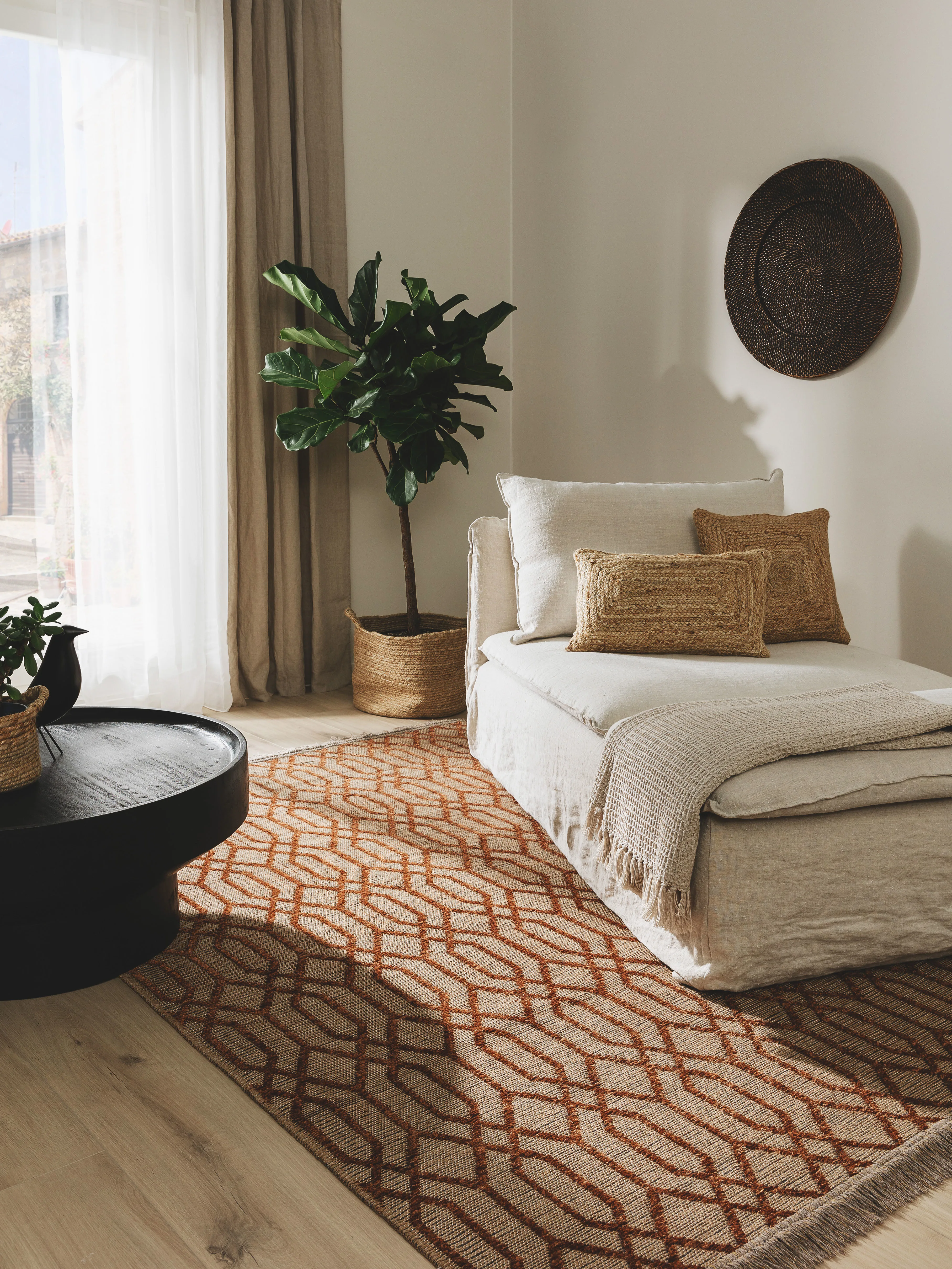 Wohnzimmer mit natürlichen Wohnaccessoires wie Jute-Kissen, Körbe aus Hampf und einem Teppich in Rostrot vor einem beigen Sofa