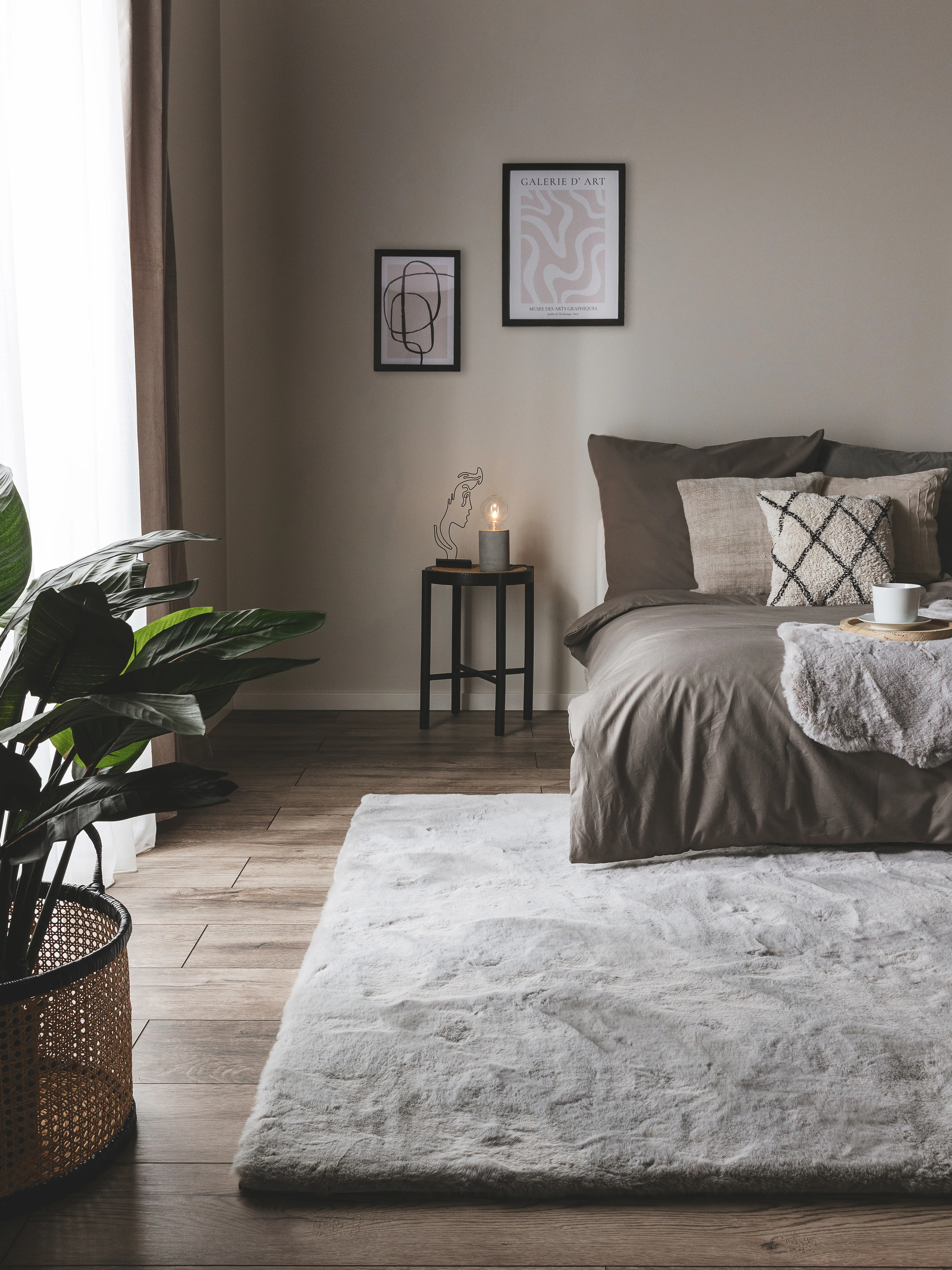 Dunkel eingerichtetes Gästezimmer mit grauer Bettwäsche, grauem Hochflorteppich als Bettvorleger und grau gestrichener Wand