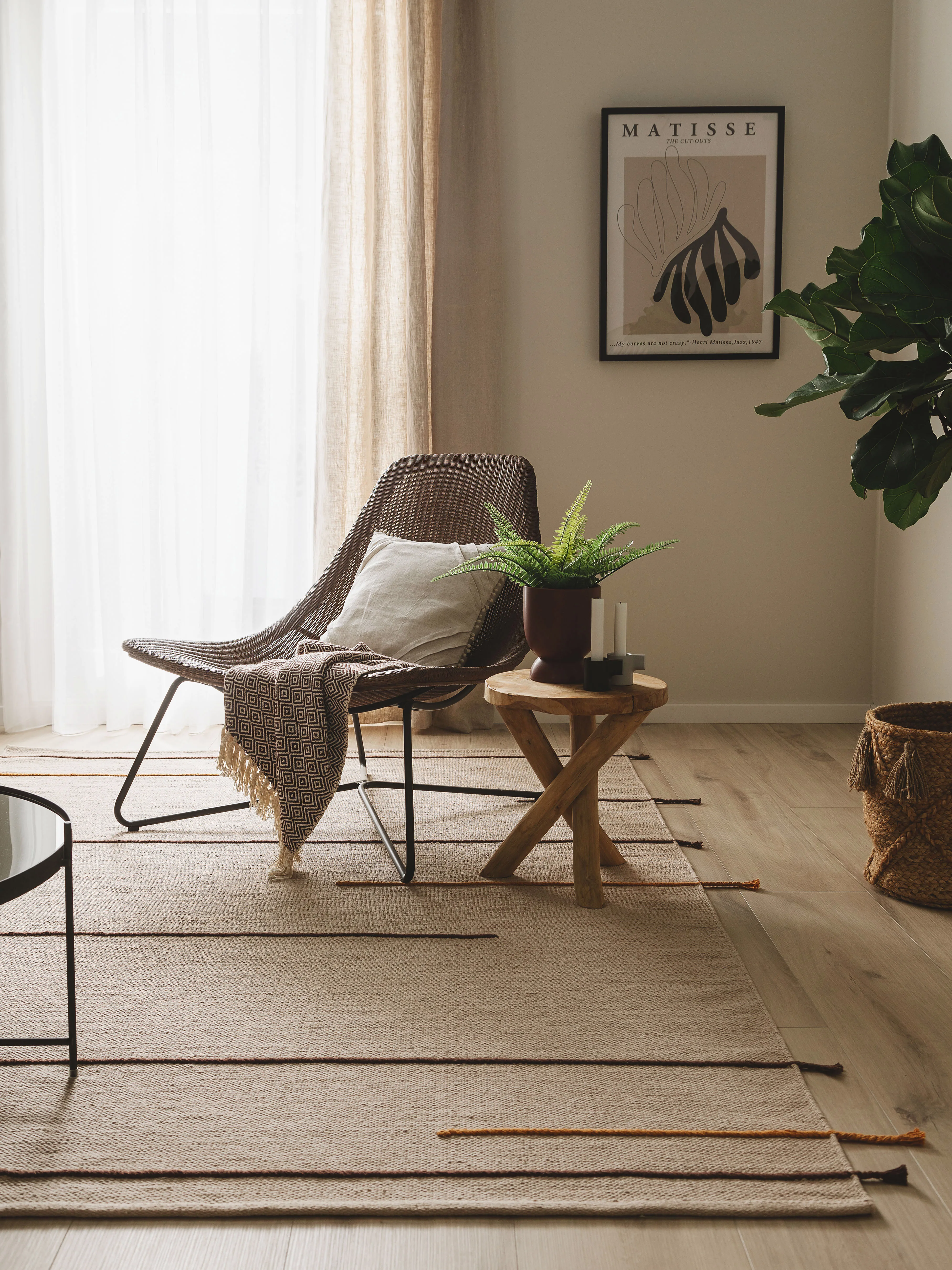Leseecke im Wohnzimmer mit einem gemütlichem Sessel inklusive Kissen und Decke, einem braunen Beistelltisch auf dem eine Pflanze steht und einem großen Teppich