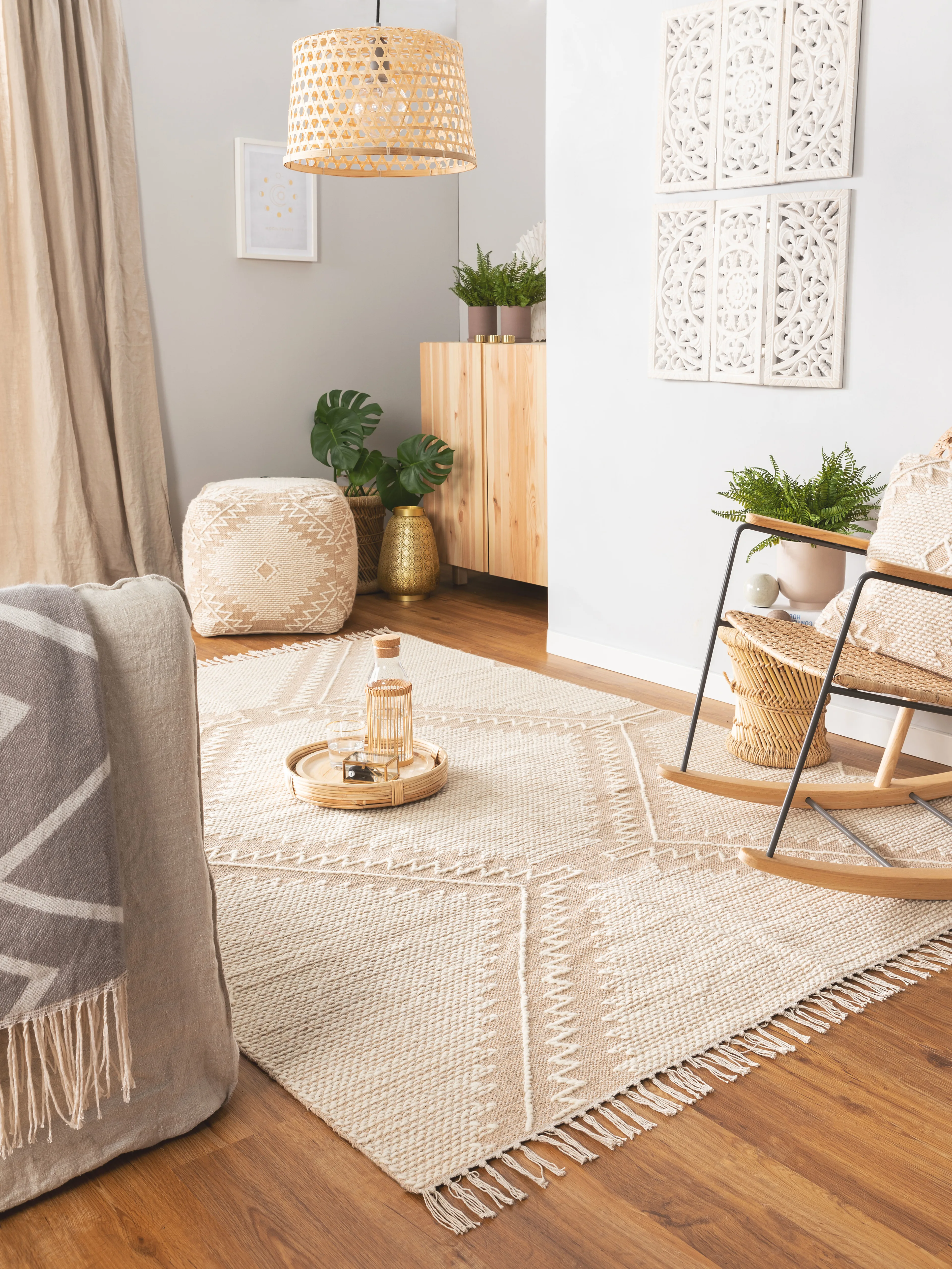 Boho-Einrichtung im Wohnzimmer mit einem verspielten Pouf, einem Teppich mit Fransen, einem Schaukelstuhl und natürlichen Details aus Bast