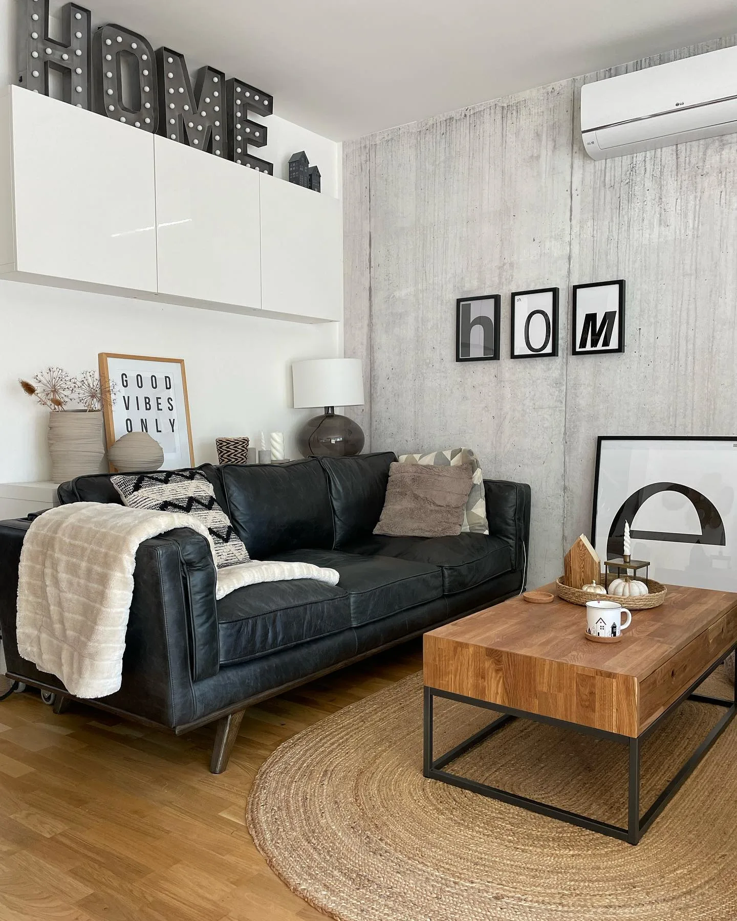 Modernes Wohnzimmer im Industrial Style mit schwarzem Ledersofa, hellbraunem Couch-Tisch aus Holz und schwarzen Bilderrahmen an der Wand