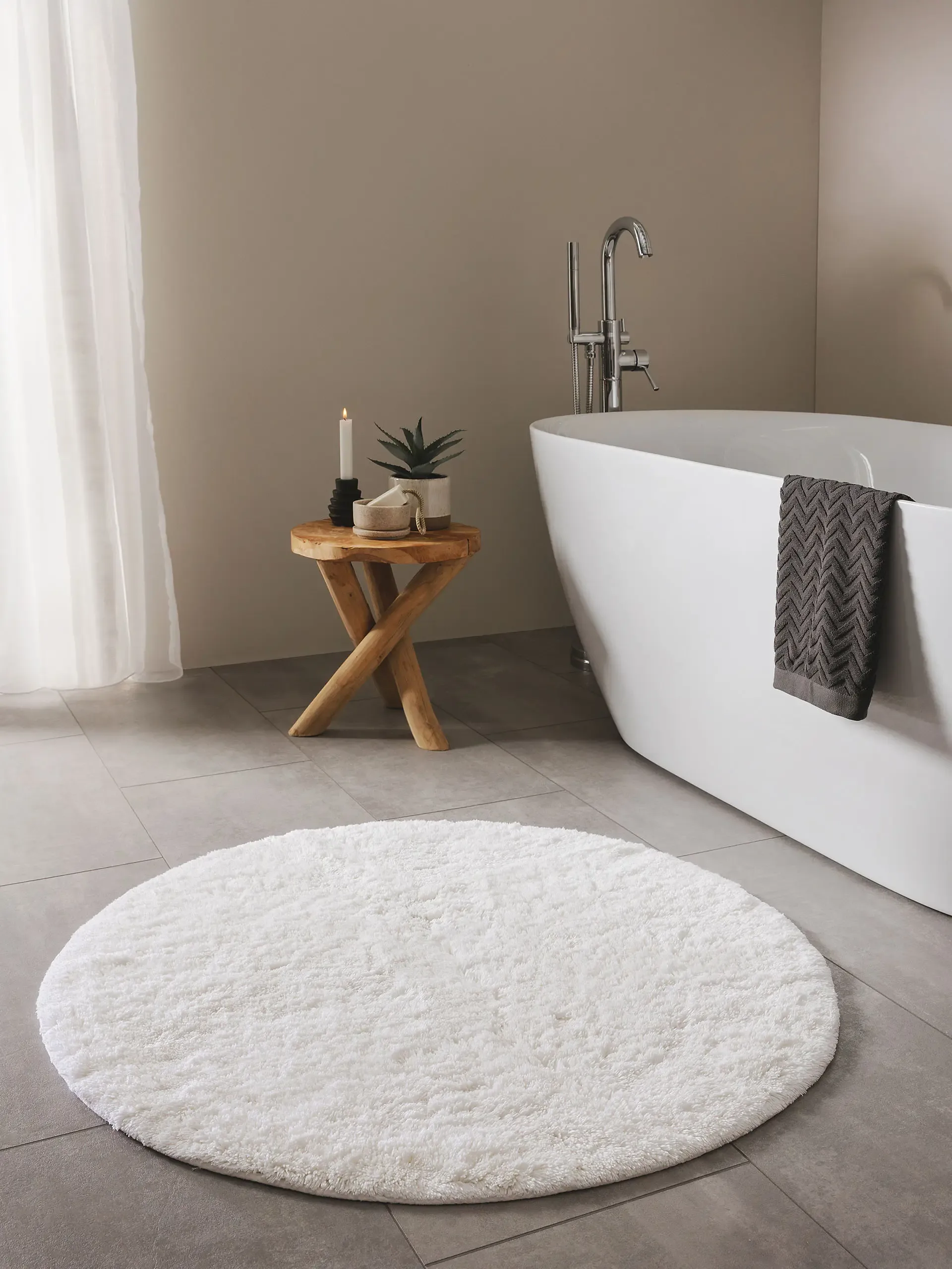 Kleines Badezimmer mit freistehender Badewanne und warmer Fußbodenheizung, in dem ein runder Badteppich mit weichen Flor liegt