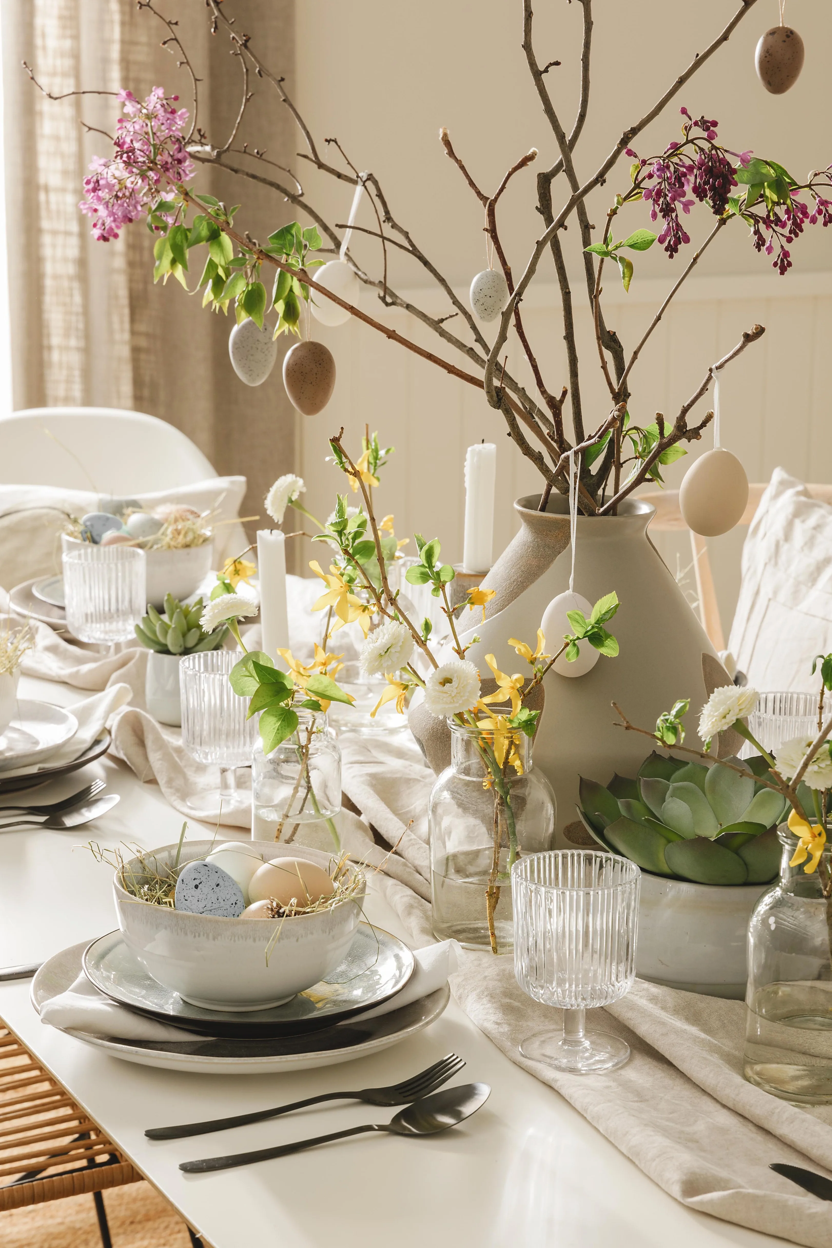 Frühlingsdeko auf dem Esstisch mit Ostereiern, Frühlingsblumen und kleinen, durchsichtigen Glasvasen