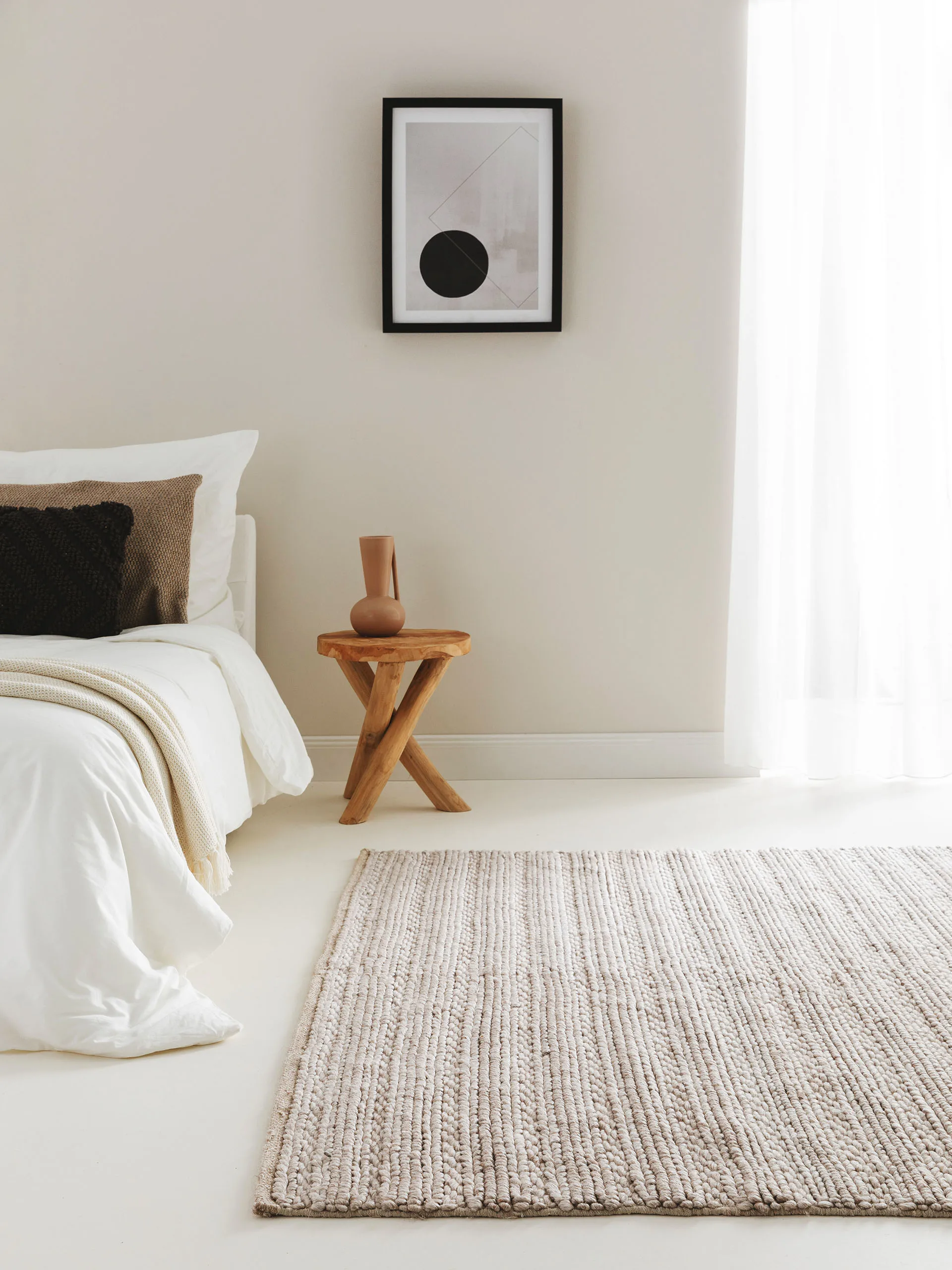 Waschbarer Schlafzimmerteppich als Bettvorleger vor einem Bett mit heller Bettwäsche, neben dem ein rustikaler Nachttisch aus Holz steht