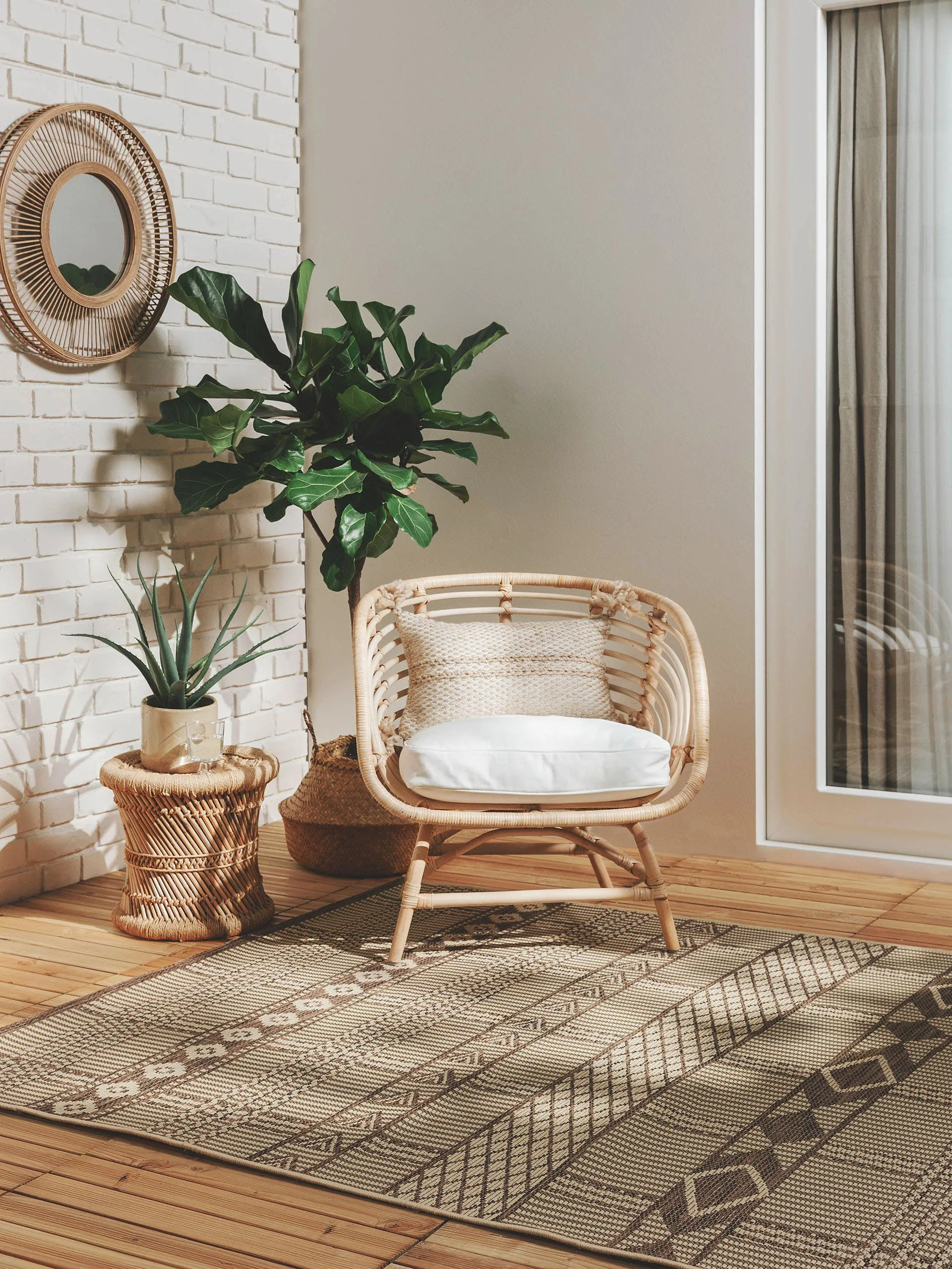 Kleine Sitzecke auf der Terrasse mit Rattansessel, Rattanbeistelltisch und Outdoor-Teppich im Boho-Design für Staycation zuhause