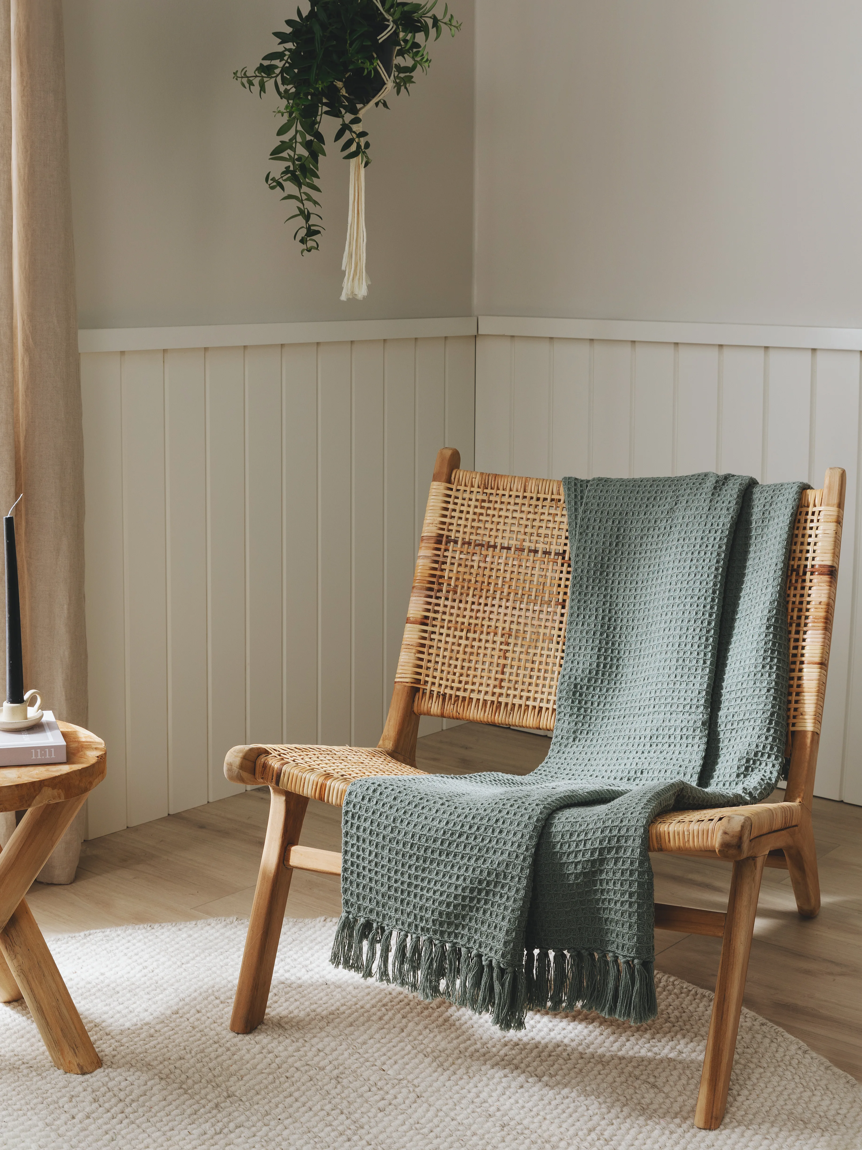 Gemütlich eingerichtete Sitzecke im Gästezimmer mit Rattansessel, mintgrüner Decke und Hängepflanze