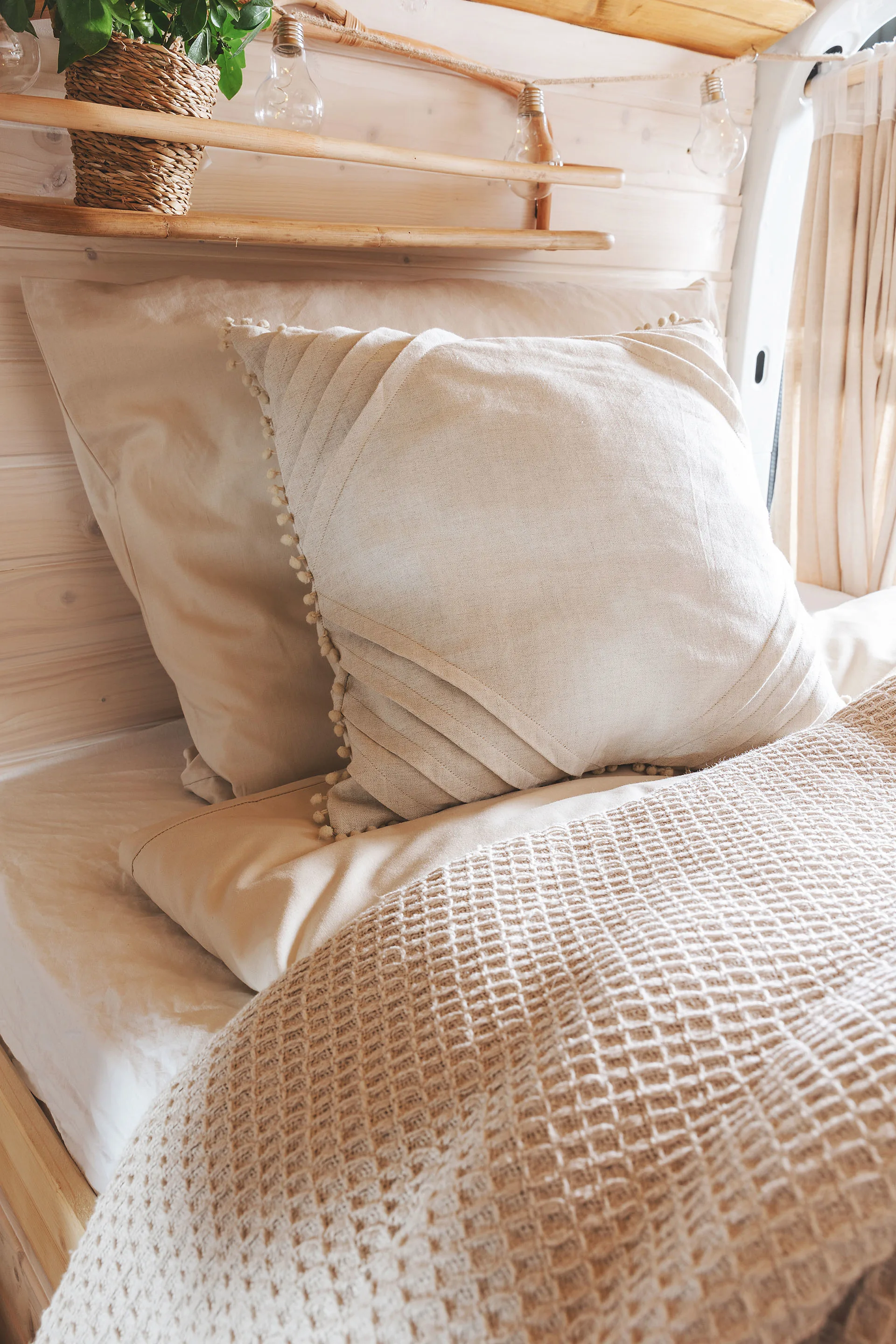 Detailaufnahme vom Bett im Van mit zwei beigen Kissen und einer beigen Tagesdecke