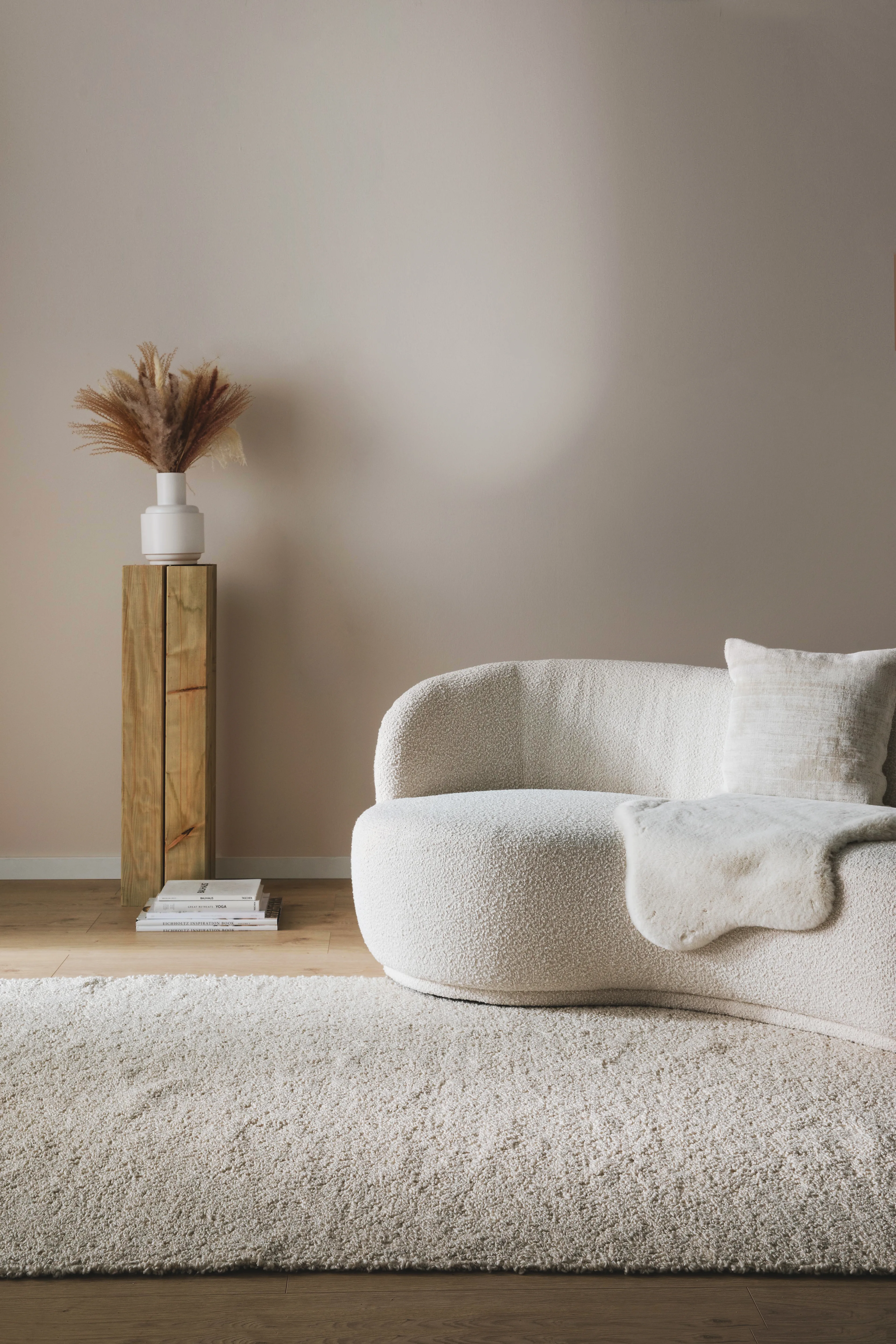 Minimalistich eingerichtetes Wohnzimmer mit einer beigen Couch, einem hellen Hochflorteppich und einem Beistelltisch au Holz mit einer Vase