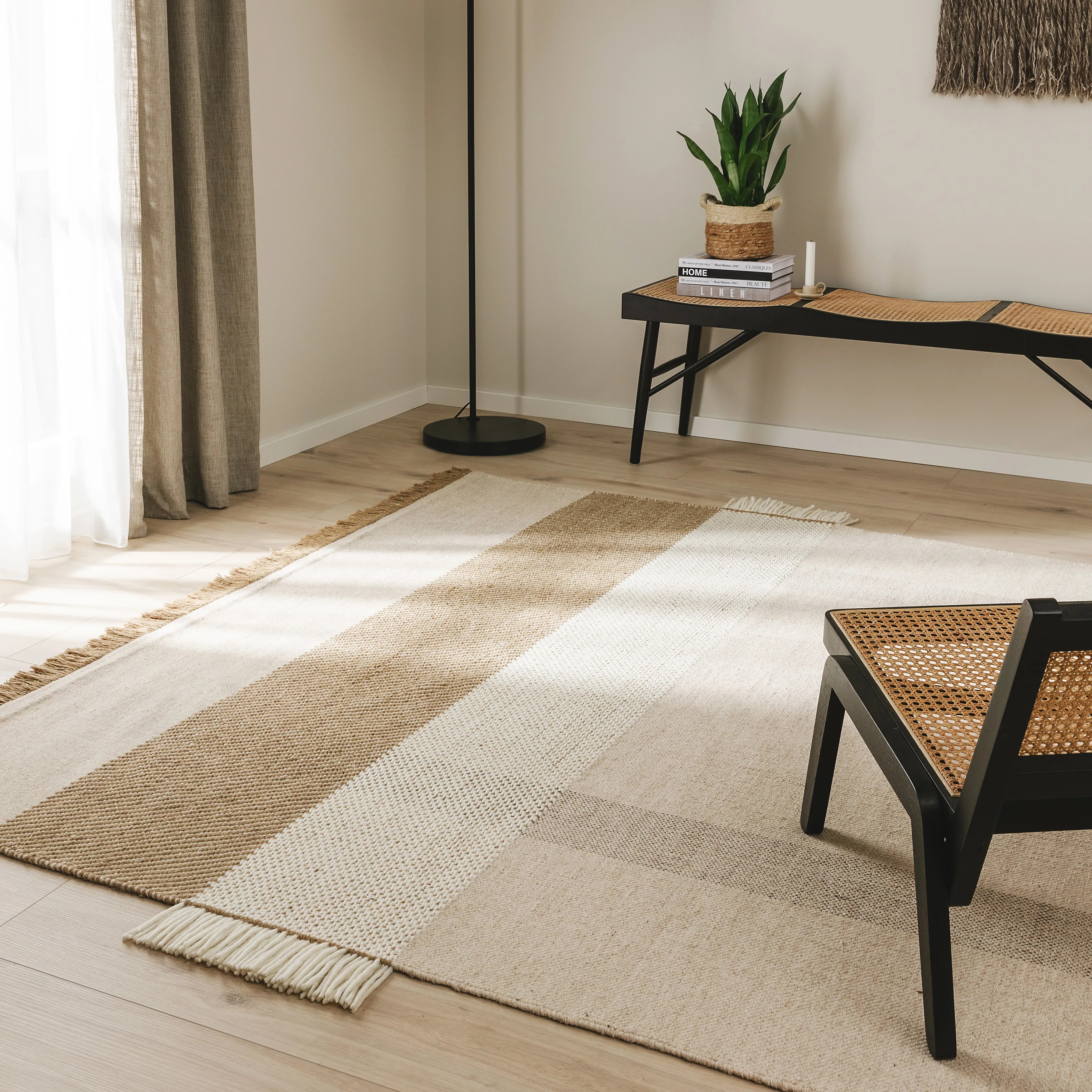 Flachgewebter Teppich in Braun, Beige und Grau mit Fransen unter einem schwarzen Rattansessel für ein gemütliches Ambiente im Wohnzimmer