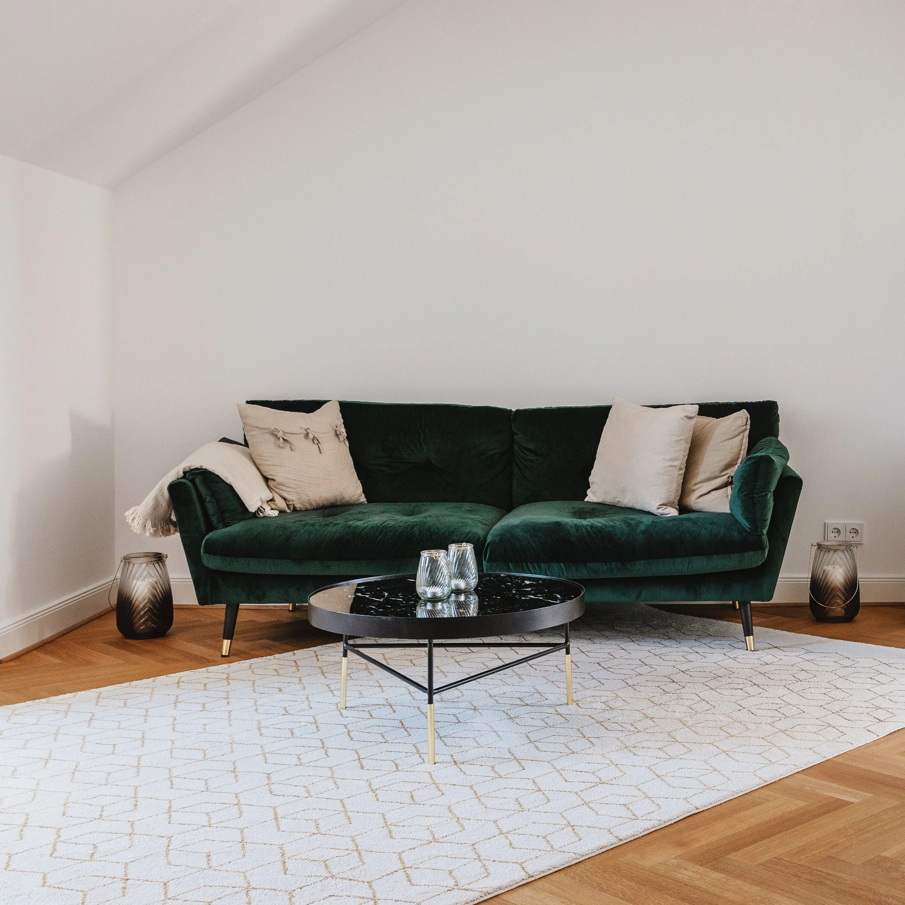 Bild von einem Wohnzimmer bevor dem Room Makeover: Leer wirkender Ram mit einem dunkelgrünen Chelsea-Sofa, drei Dekokissen und einem hellen Teppich