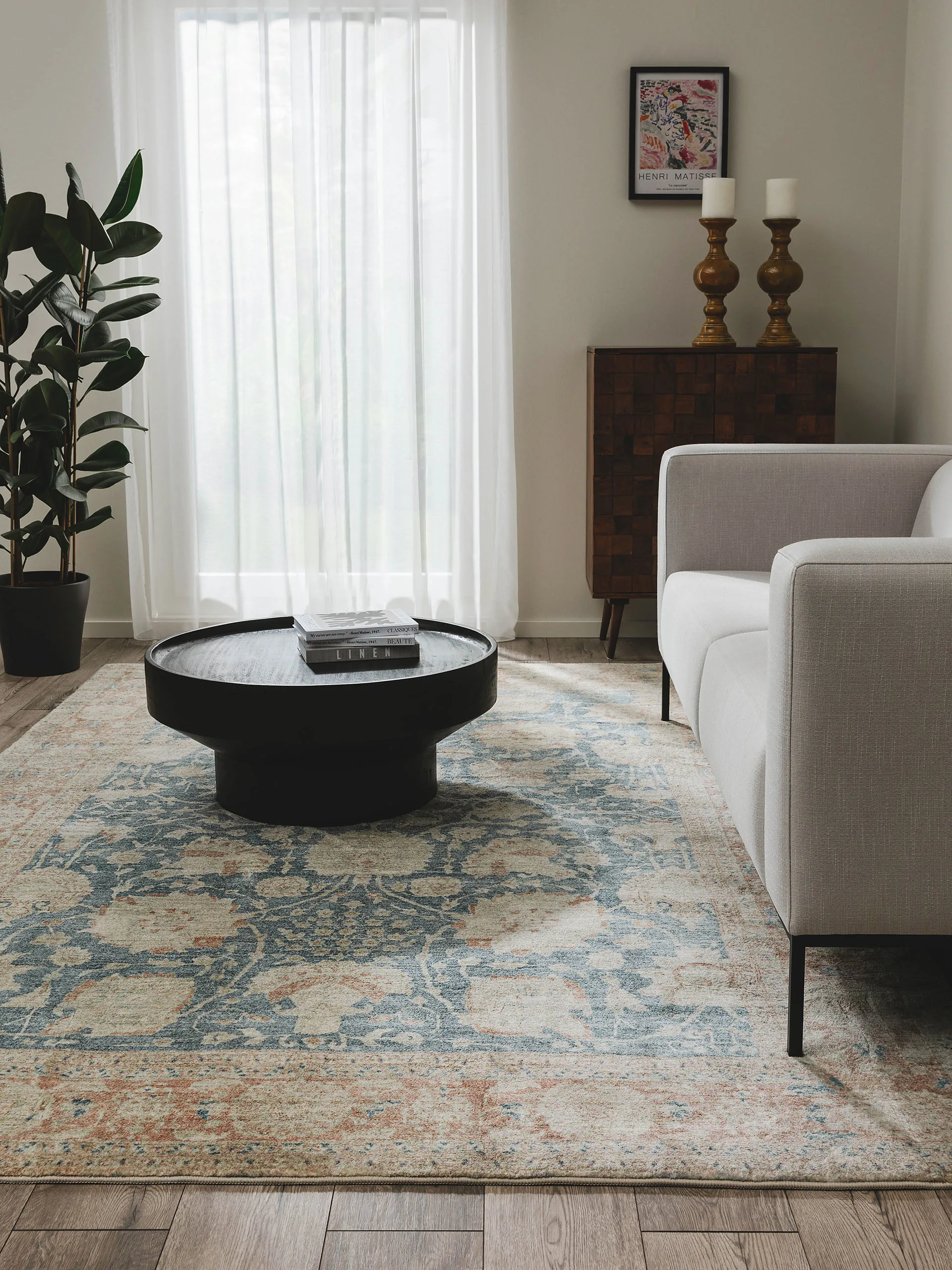 Große Topfpflanzen in einem skandinavisch eingerichtete Wohnzimmer mit Vintage-Teppich in Petrol und Rot und einem hellgrauen Zwei-Sitzer-Sofa