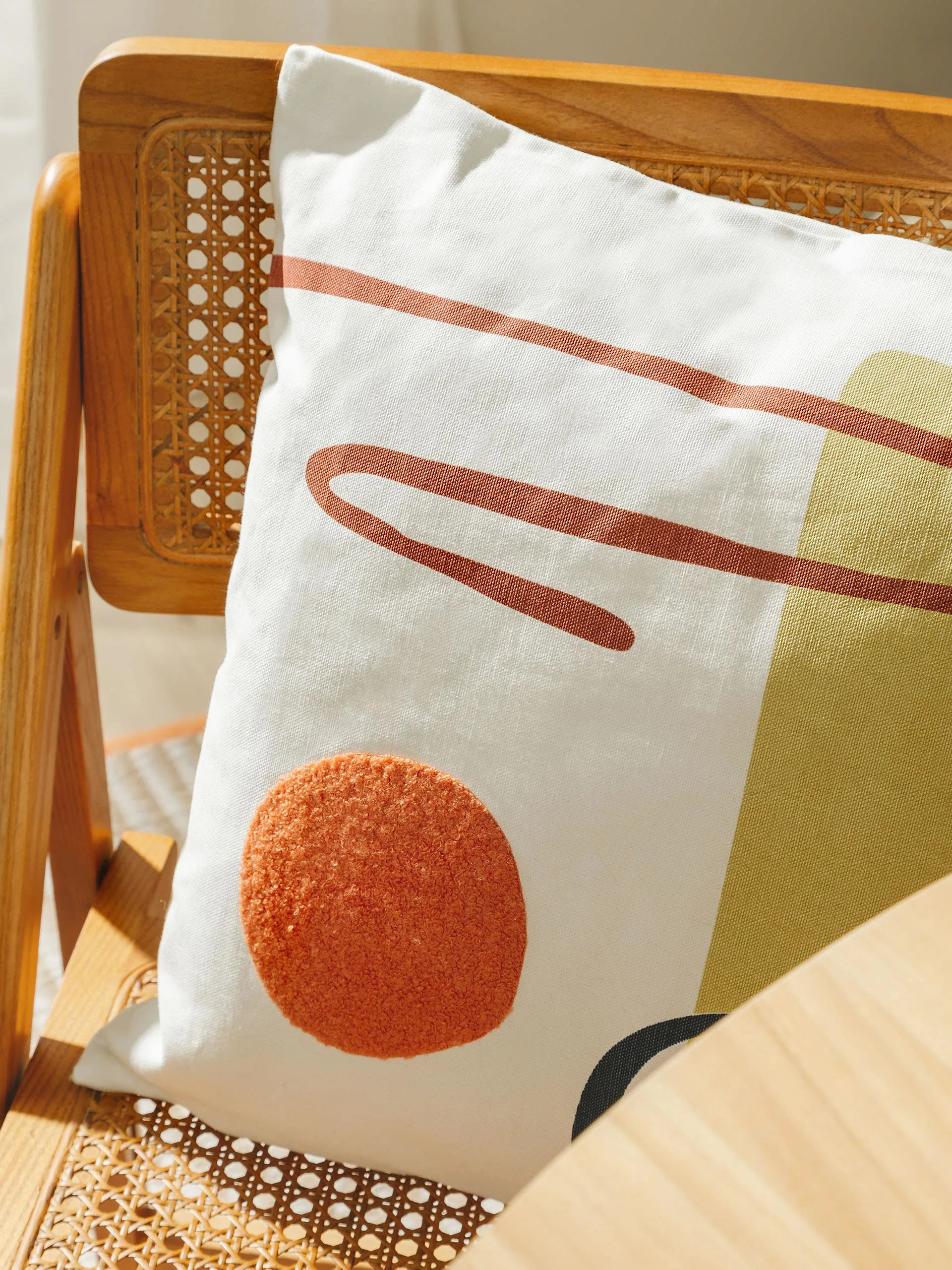 Detailaufnahme von einem Kissen mit bunten geometrischen Muster auf einem braunen Rattanstuhl