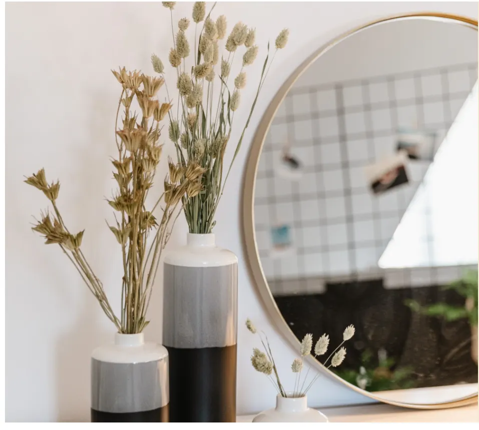 Detailaufnahme von Dekoration für ein Room Makeover: Drei Vasen mit Trockenblumen auf einem braunen Sideboard mit rundem Spiegel