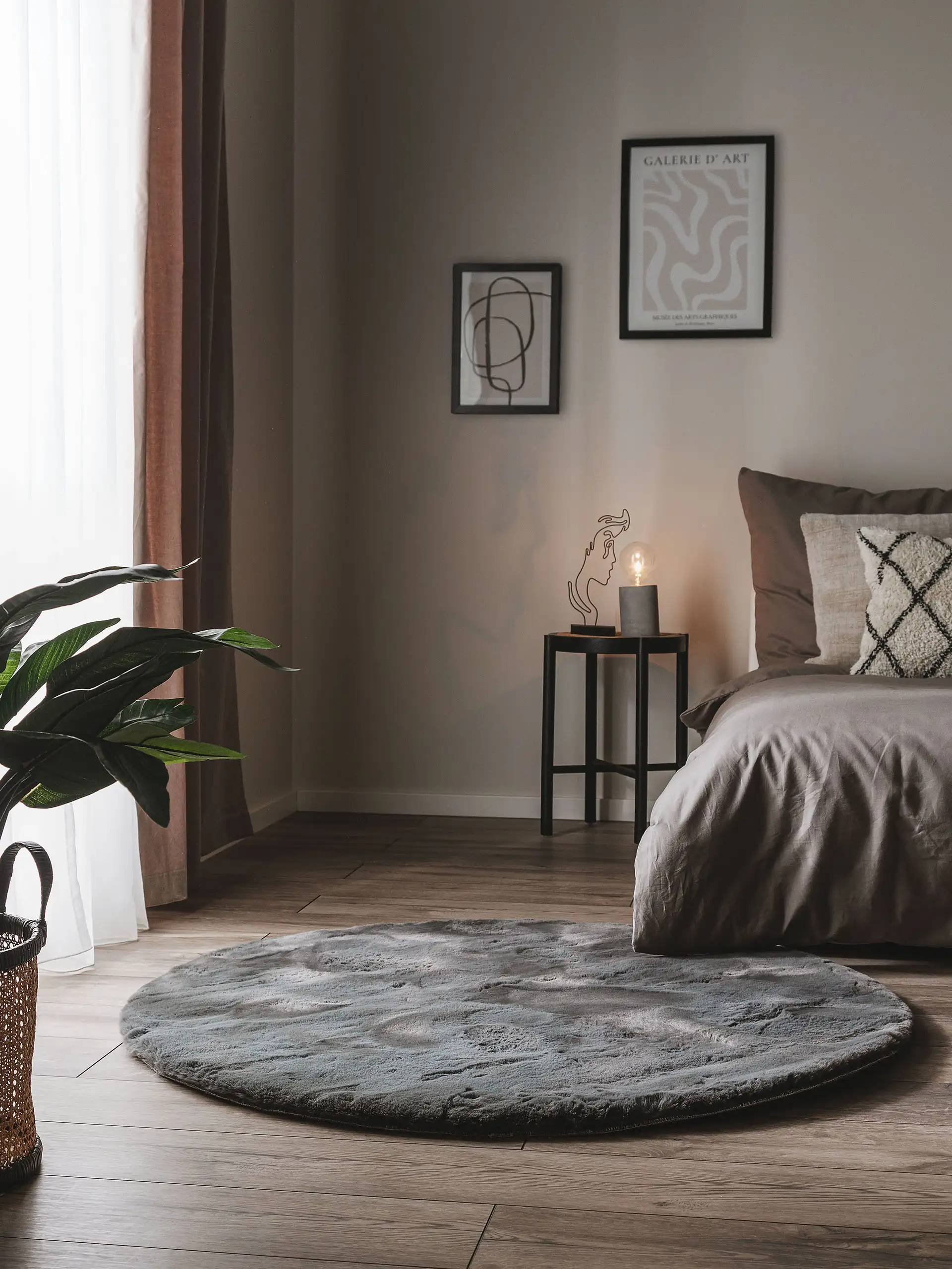 Dunkel eingerichtetes Schlafzimmer mit grauen Wänden, grauer Bettwäsche und einem dunkelgrauen, runden Teppich vor dem Bett