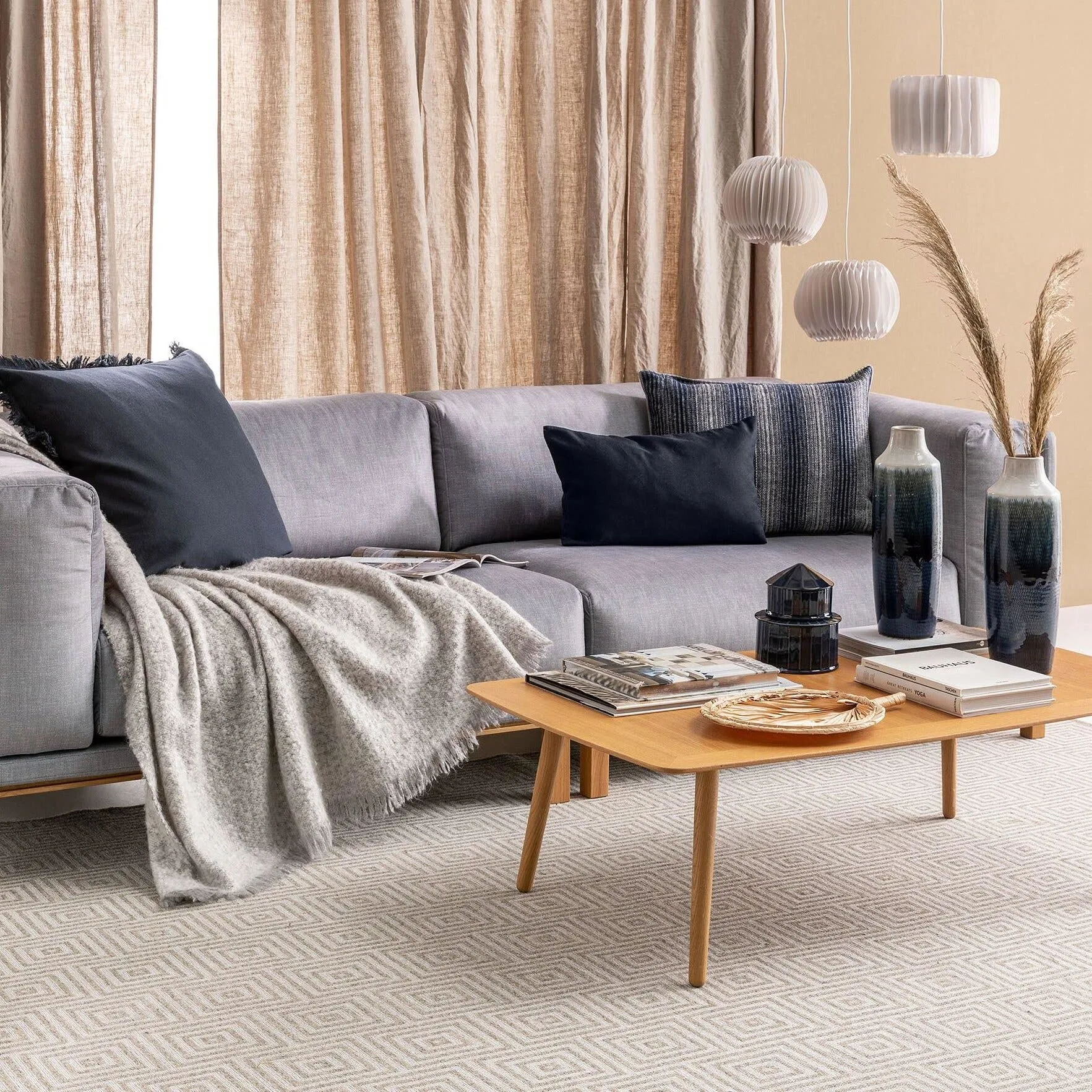 Japandi Style Wohnzimmer mit grauem Sofa und dunkelblauen Dekokissen und eine hellbraunen Couch-Tisch aus Holz, auf de dunkelbaue Vasen mit Pampasgras stehen