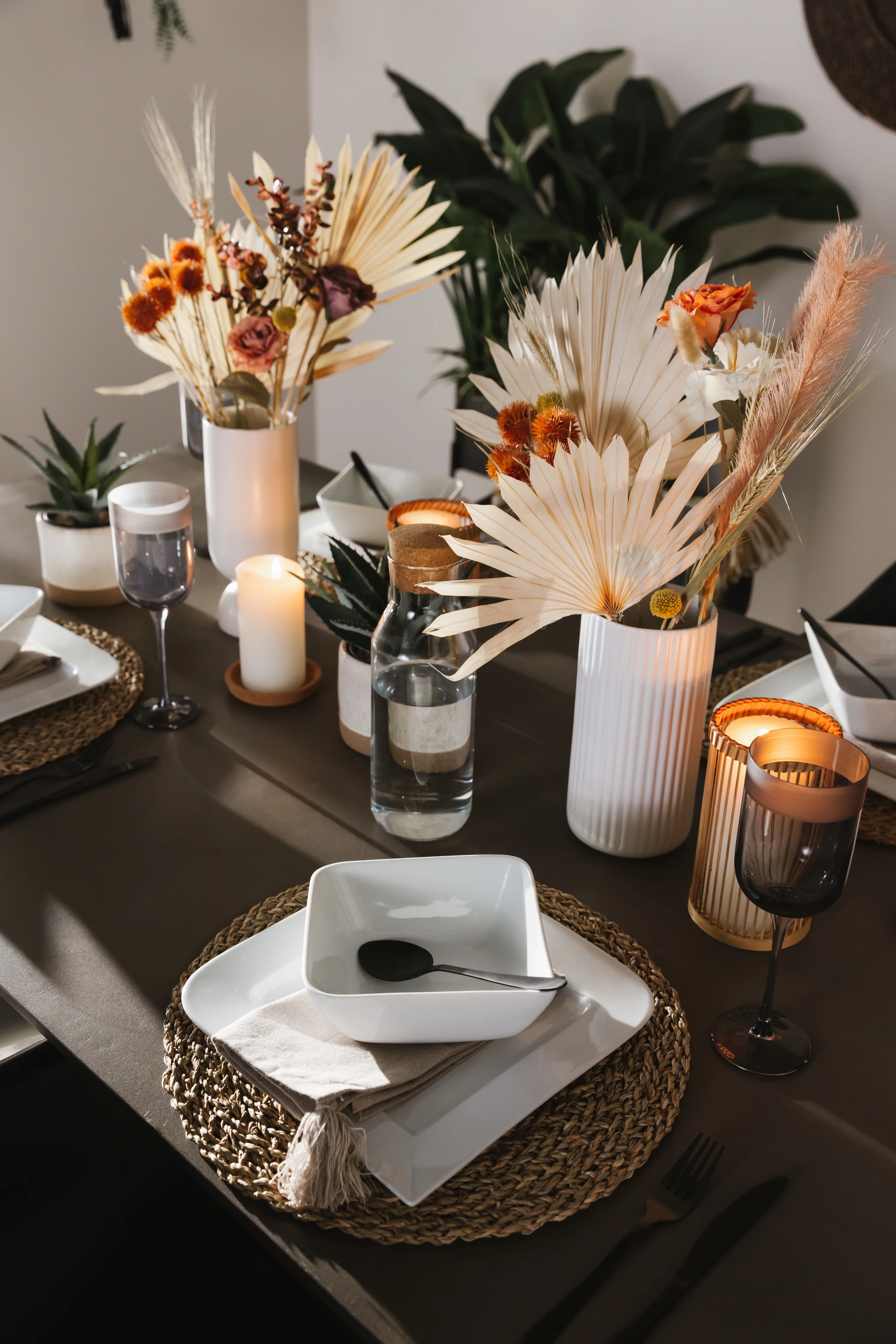Detailaufnahme von der Tischdekoration im Esszimmer mit Kerzen, Blumenvasen und Tischdeckchen aus Bast auf einem schwarzen Untergrund
