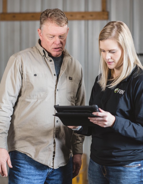 A farmer and an FBN insurance agent reviewing a tablet inside a building