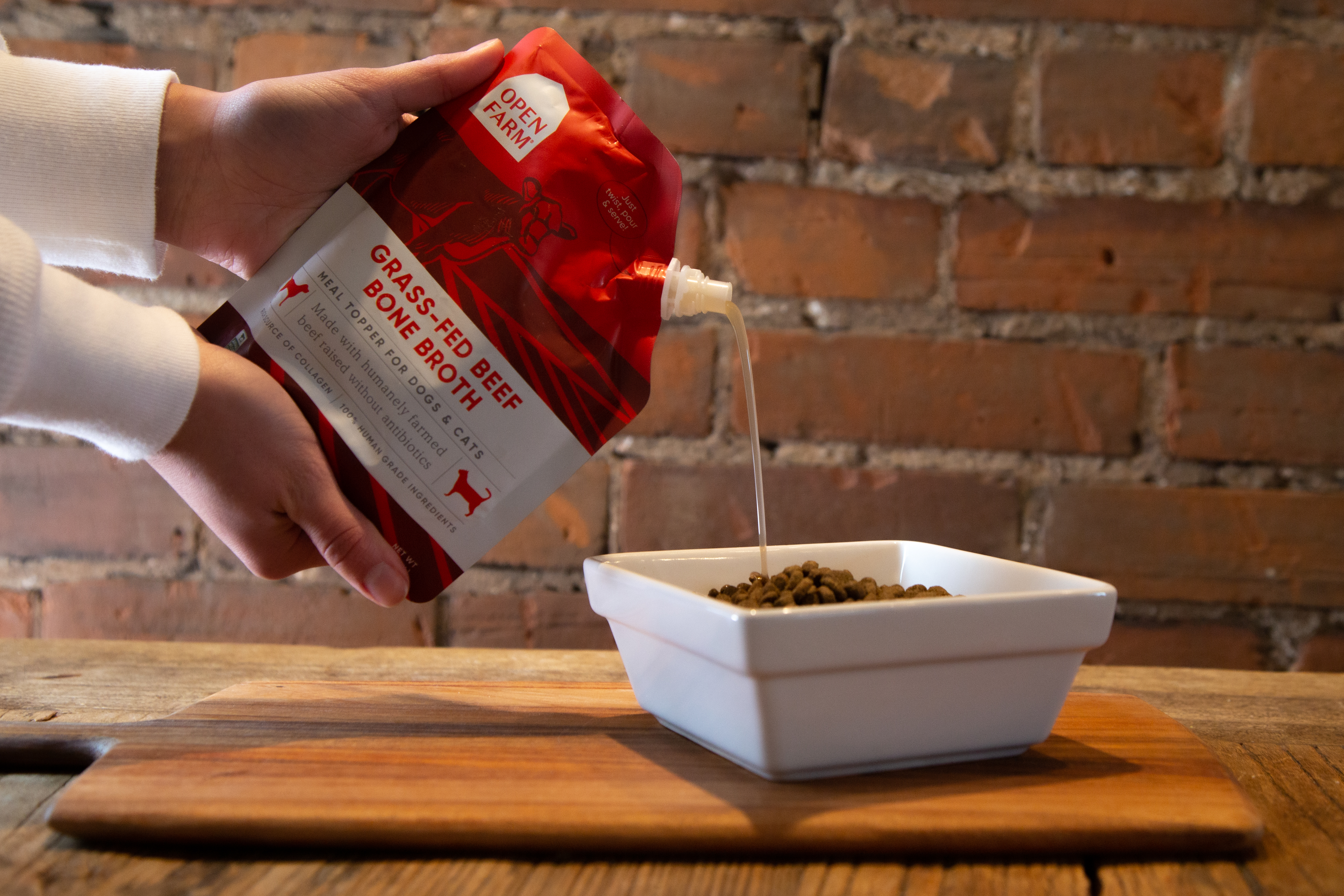 Bone broth for cats being poured into a bowl of dry food