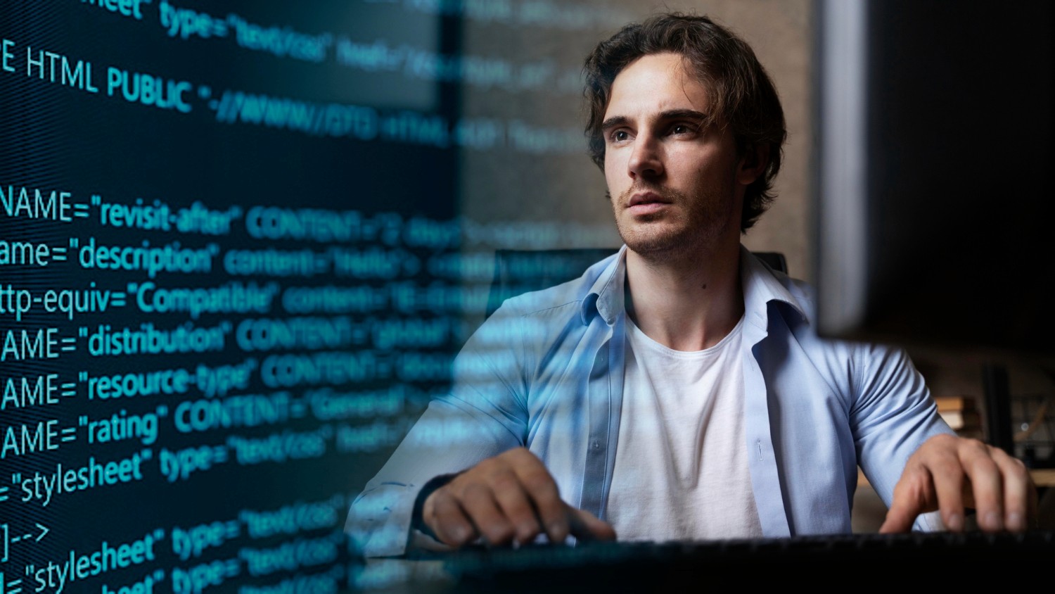 A man sits at a computer, focused on a screen displaying lines of code.