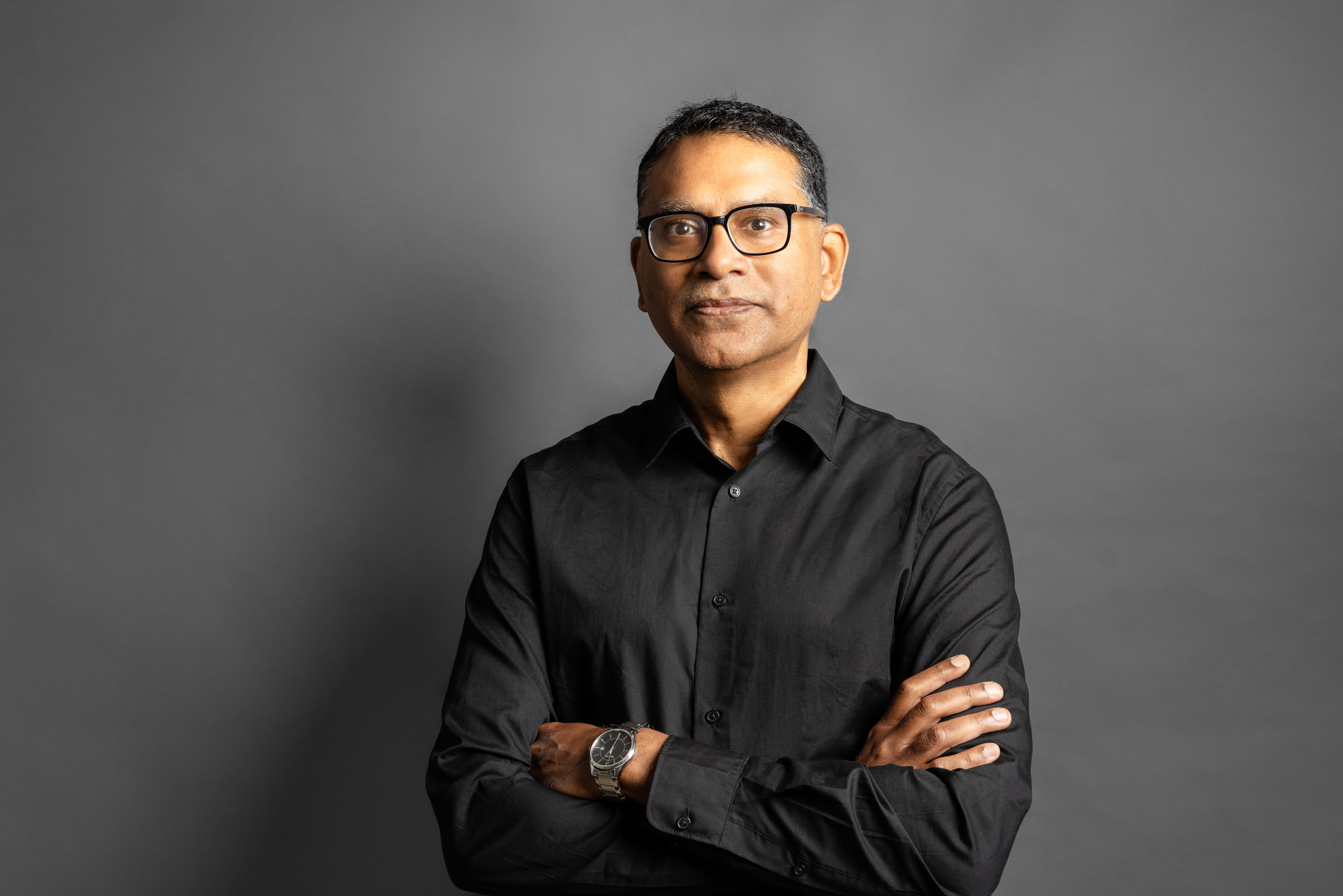 Professional portrait of a person in a black button-up shirt with arms crossed against a gray background.