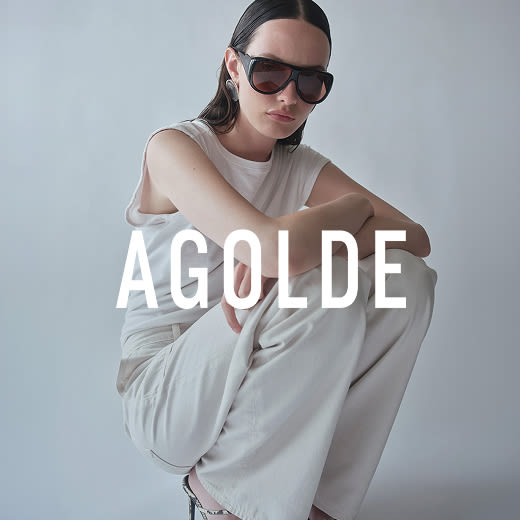 Model crouches wearing a white tank top and trousers against a white background.