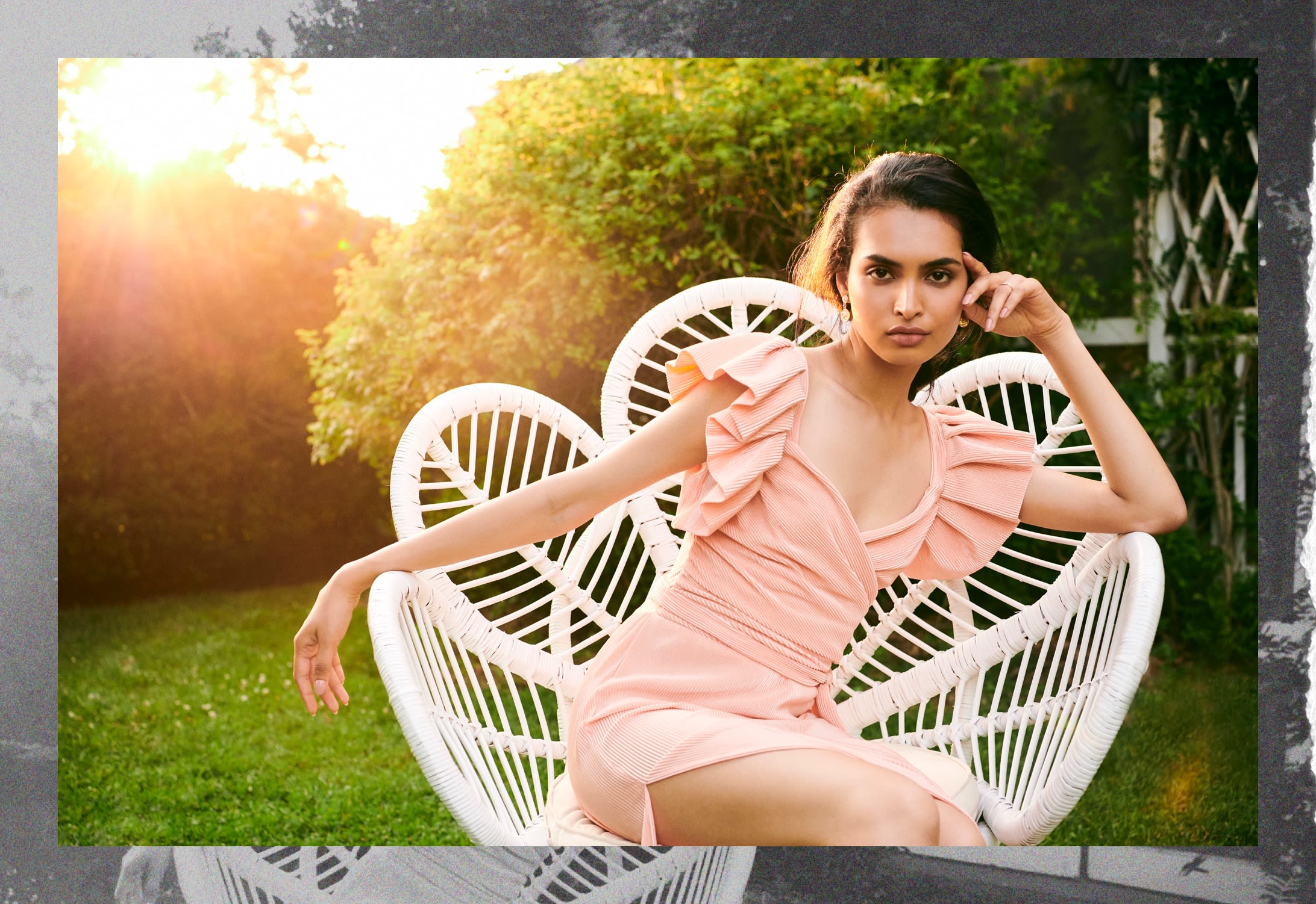 Model in pink, pleated party dress sitting in a white chair.