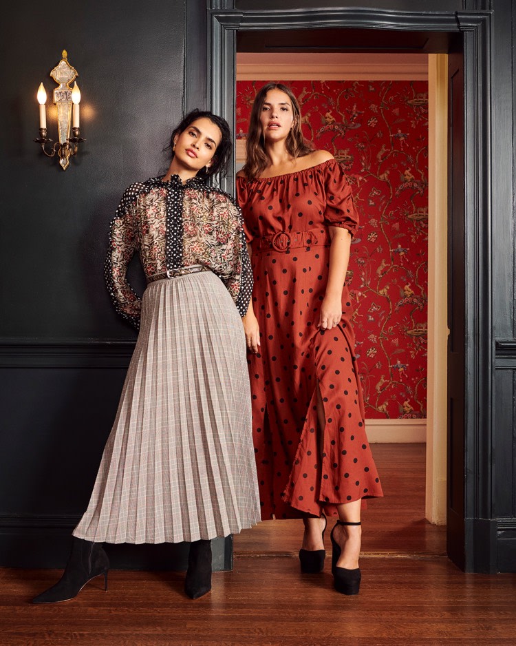 Models wearing mixed prints in a room with black walls and colorful wallpaper.