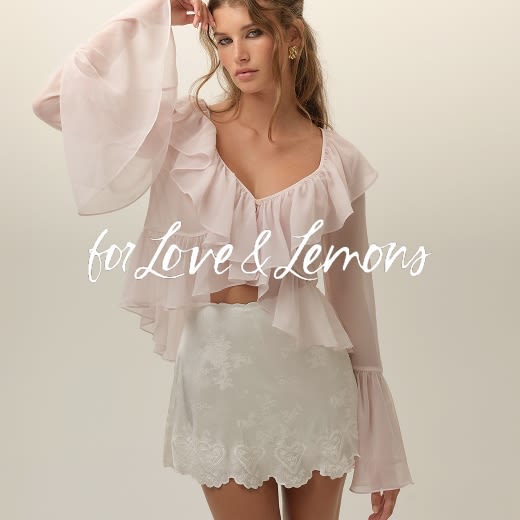 Model in a light pink blouse with bell sleeves and a white high rise eyelet skirt.