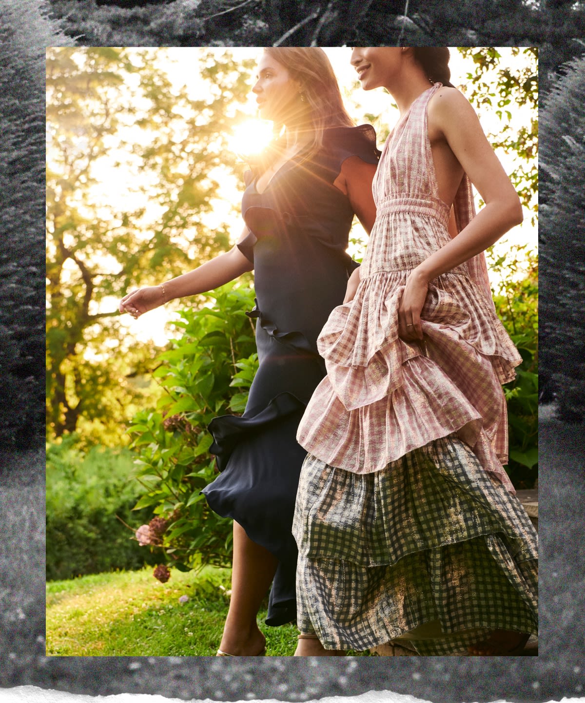 Two models wearing shimmery tiered dress and and a navy ruffle dress walking through a garden.